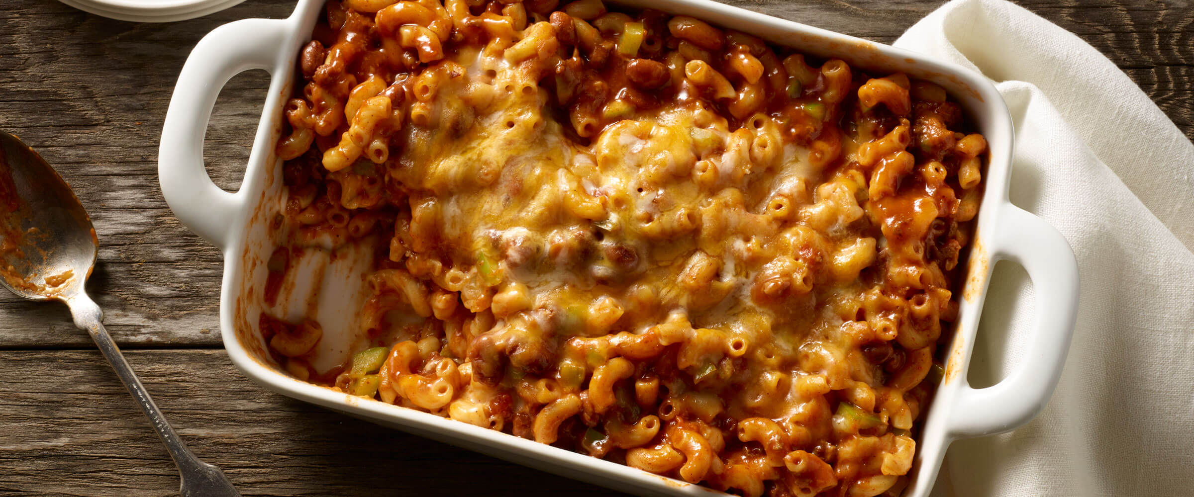 Chili Mac ‘n’ Cheese Bake in white dish with serving spoon and white linen