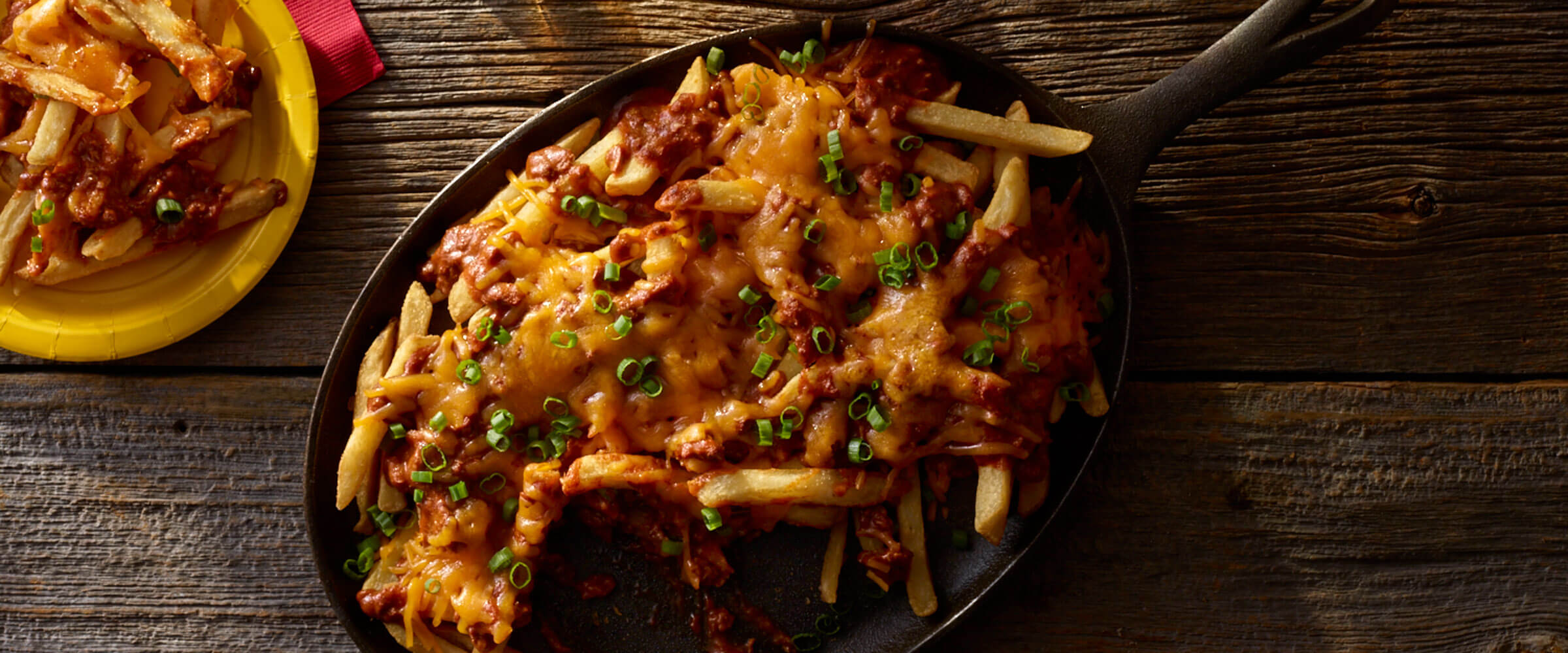 Chili Cheese Fries topped with green onion in skillet on wood table