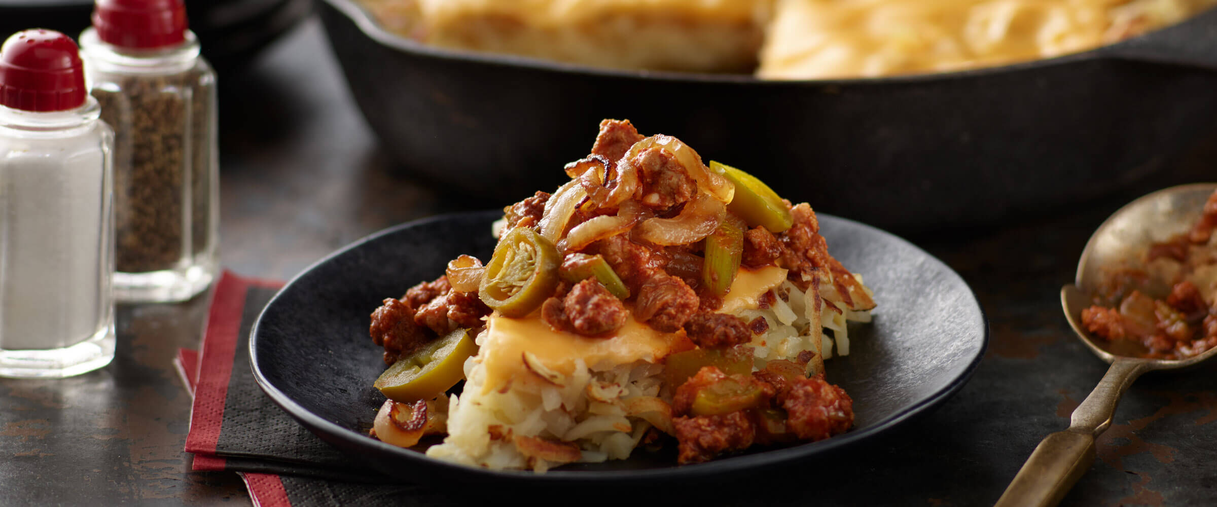 Creole Dirty Bird Chili Hash topped with cheese and jalapenos on a black plate with salt and pepper shakers on the side