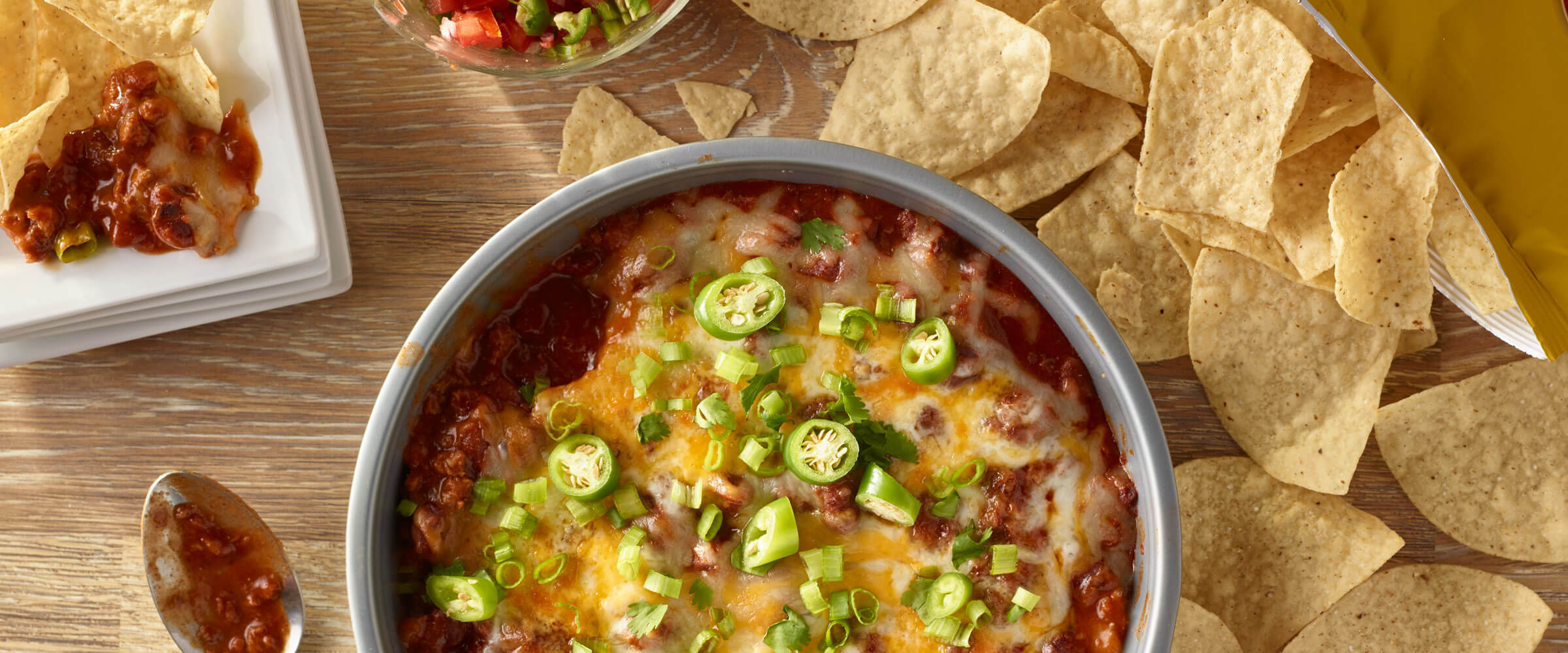 Easy Chili Cheesy Dip in gray bowl topped with jalapenos and green onions with chips on side