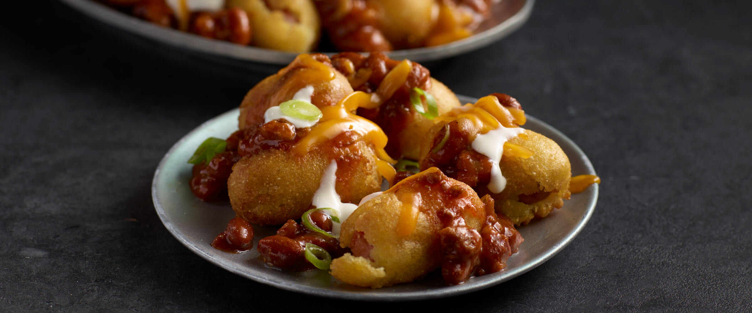 Hot Chili Cheese Corn Dog Bites topped with cheese and sour cream on a plate