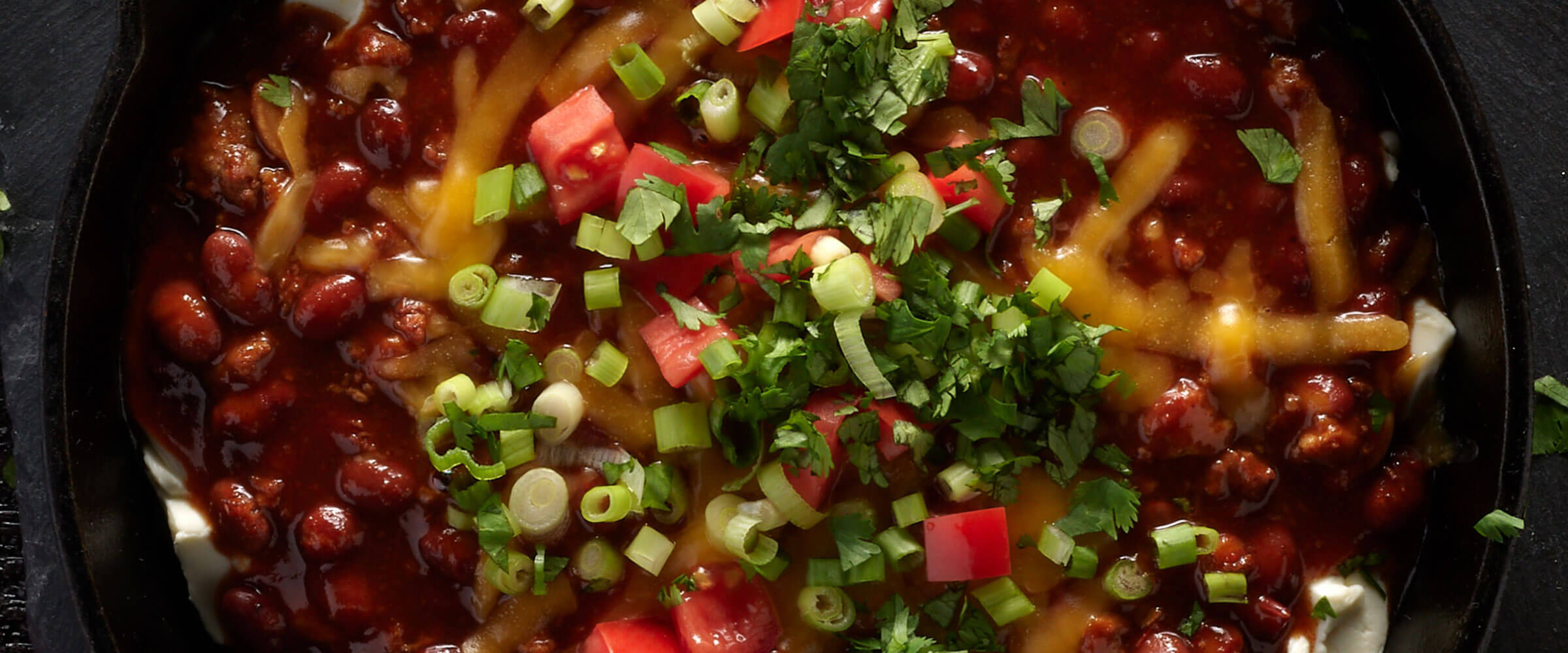 Hot Chili Cheese Dip in black bowl topped with tomato, green onion and cilantro