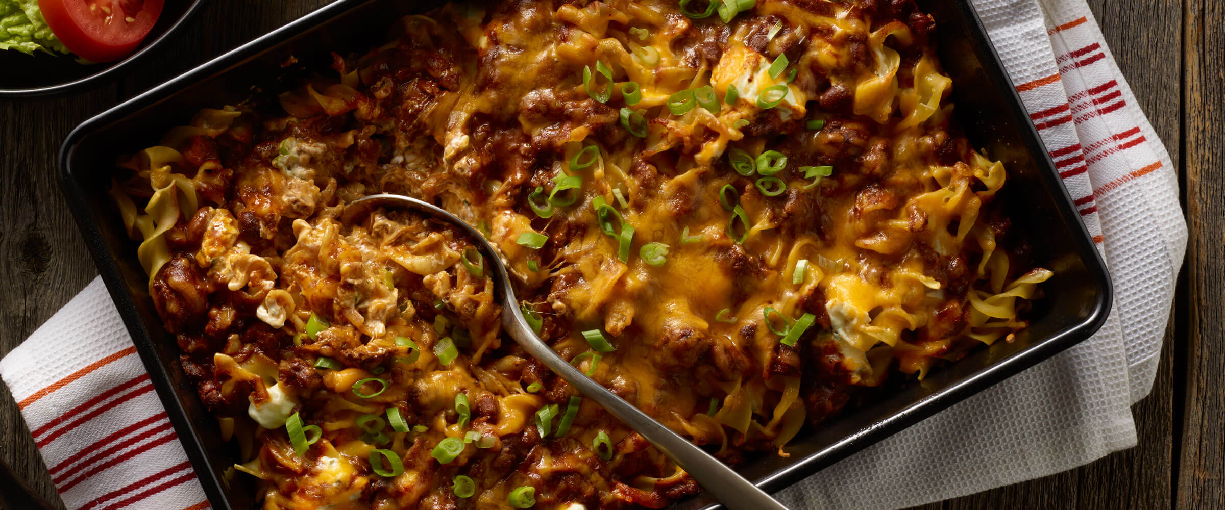Layered Southwest Chili Mac Bake in black dish topped with cheese and green onions on linen
