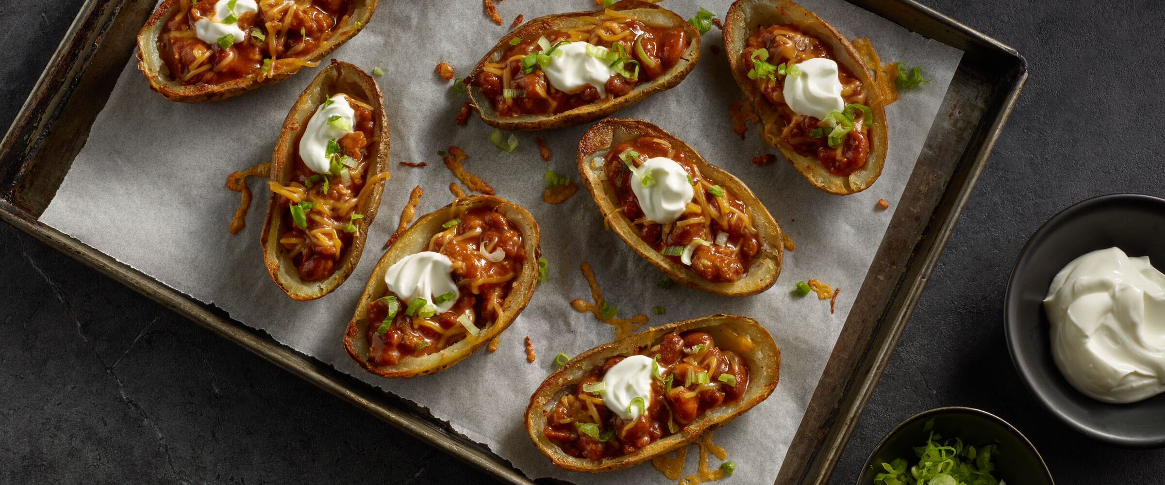 Loaded Baked Potato Skins topped with sour cream on sheet pan