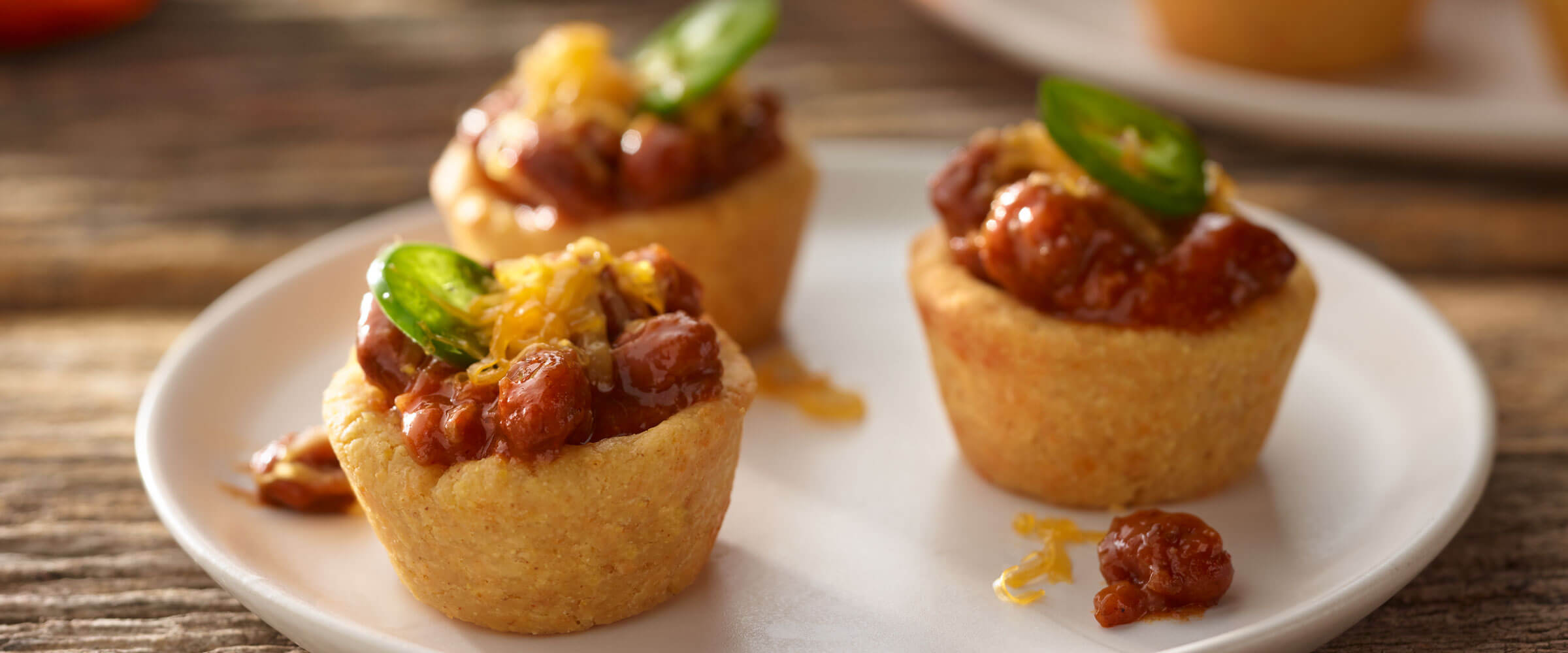 Mini Chili Cornbread Bites topped with cheese and jalapeno on a white plate