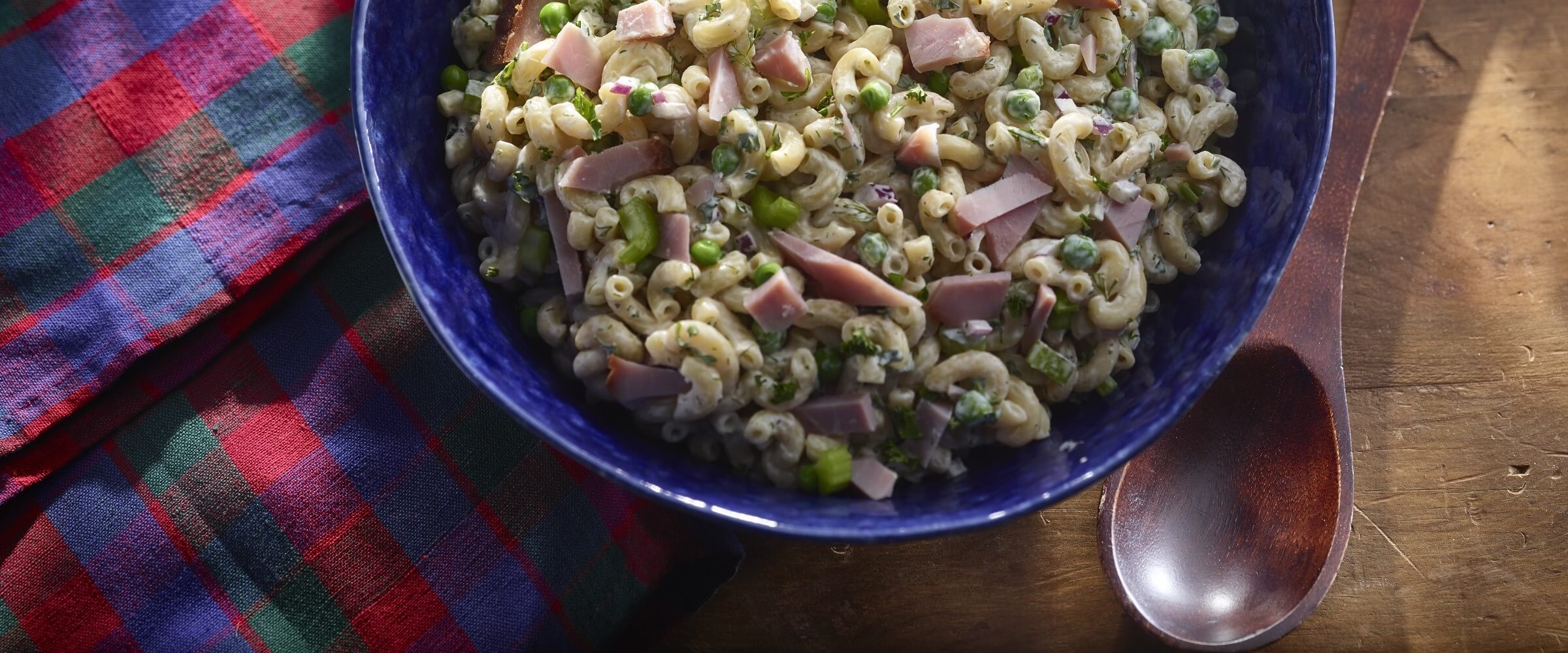 classic macaroni salad with ham in blue bowl with plaid napkin