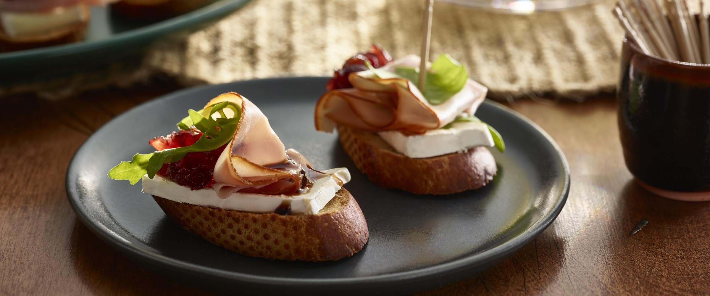 ham cranberry brie crostini with balsamic glaze on gray plate