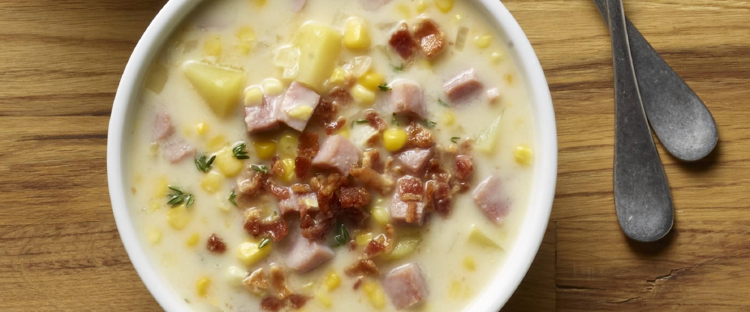 Ham potato corn chowder topped with bacon bits in white bowl
