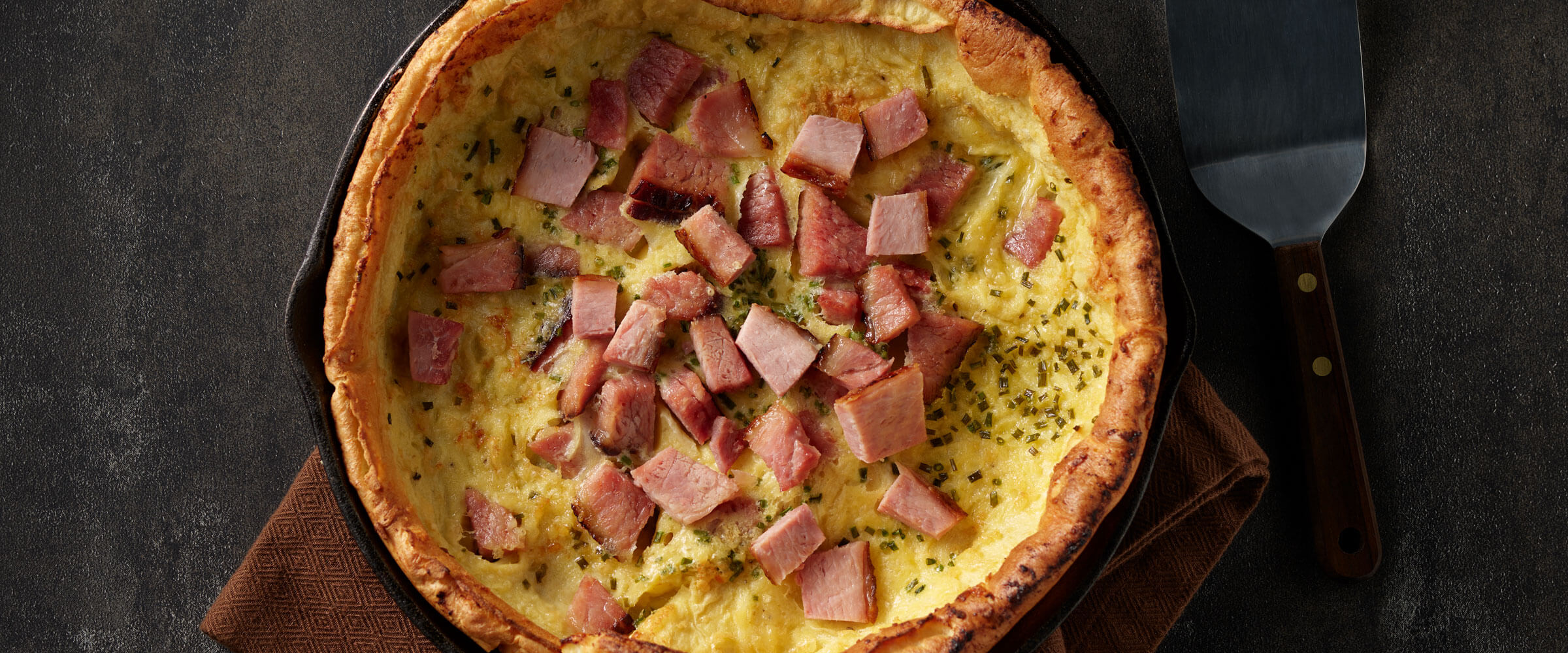 Savory Dutch Baby Pancake with Ham and Eggs in cast iron skillet with spatula
