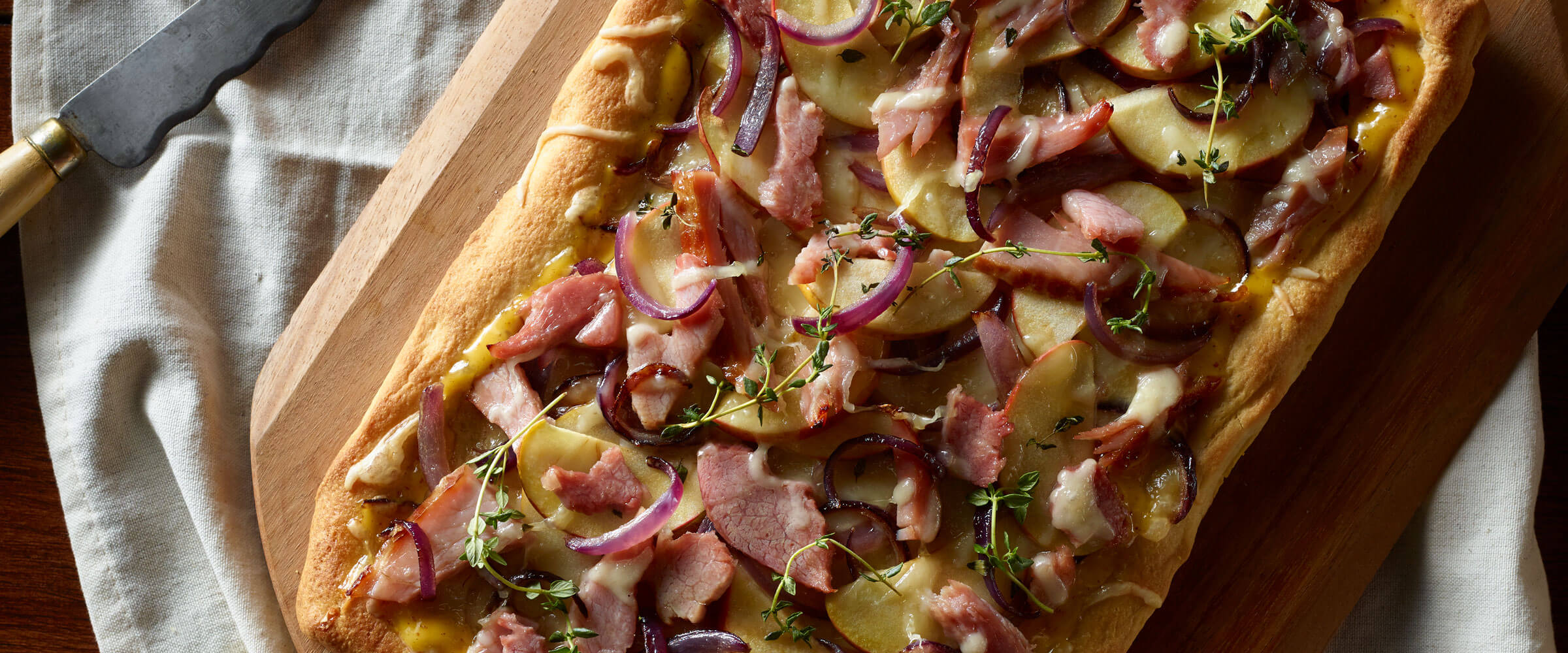 Ham and Apple Caramelized Onion Flatbread on wood cutting board with linen
