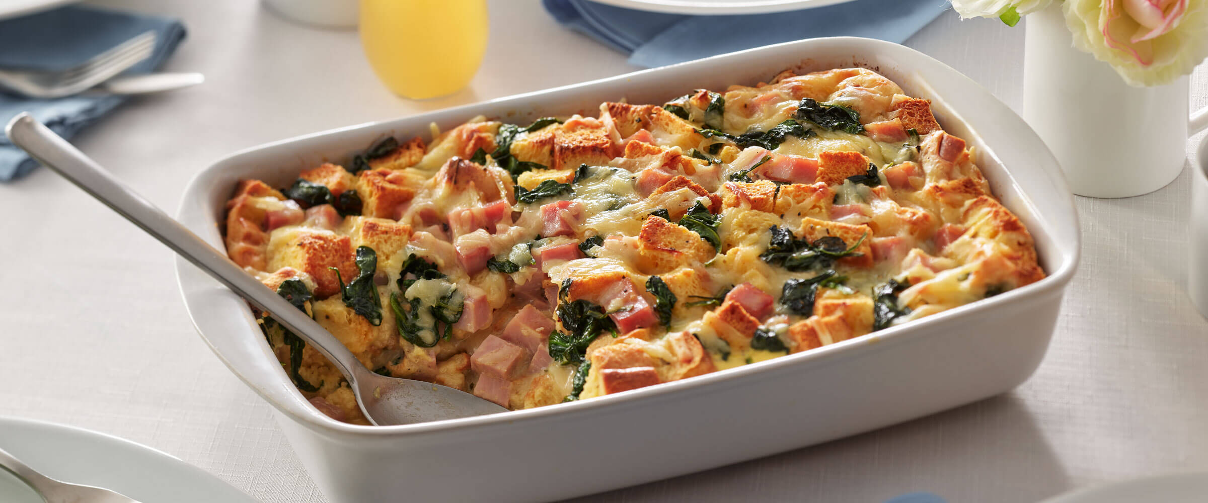 Ham, Spinach and Gruyere Strata in white dish with serving spoon