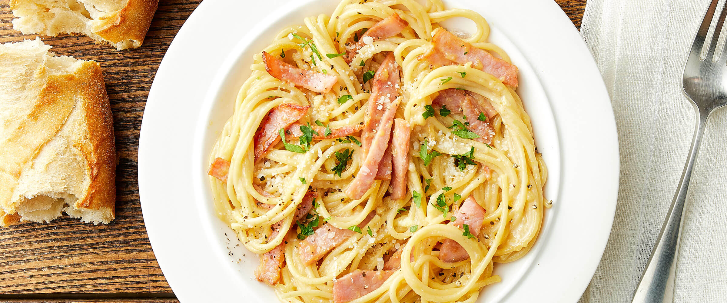Ham Carbonara in white bowl with crusty bread on side