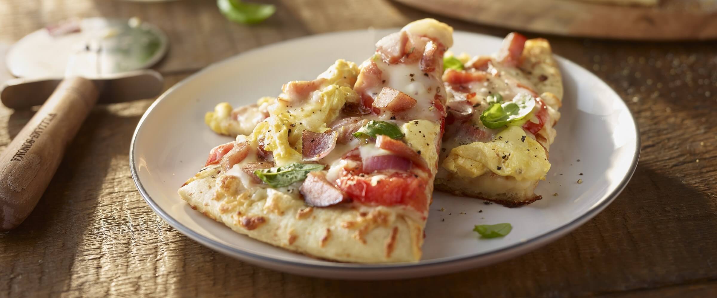 Breakfast pizza slices with ham and bacon on white plate