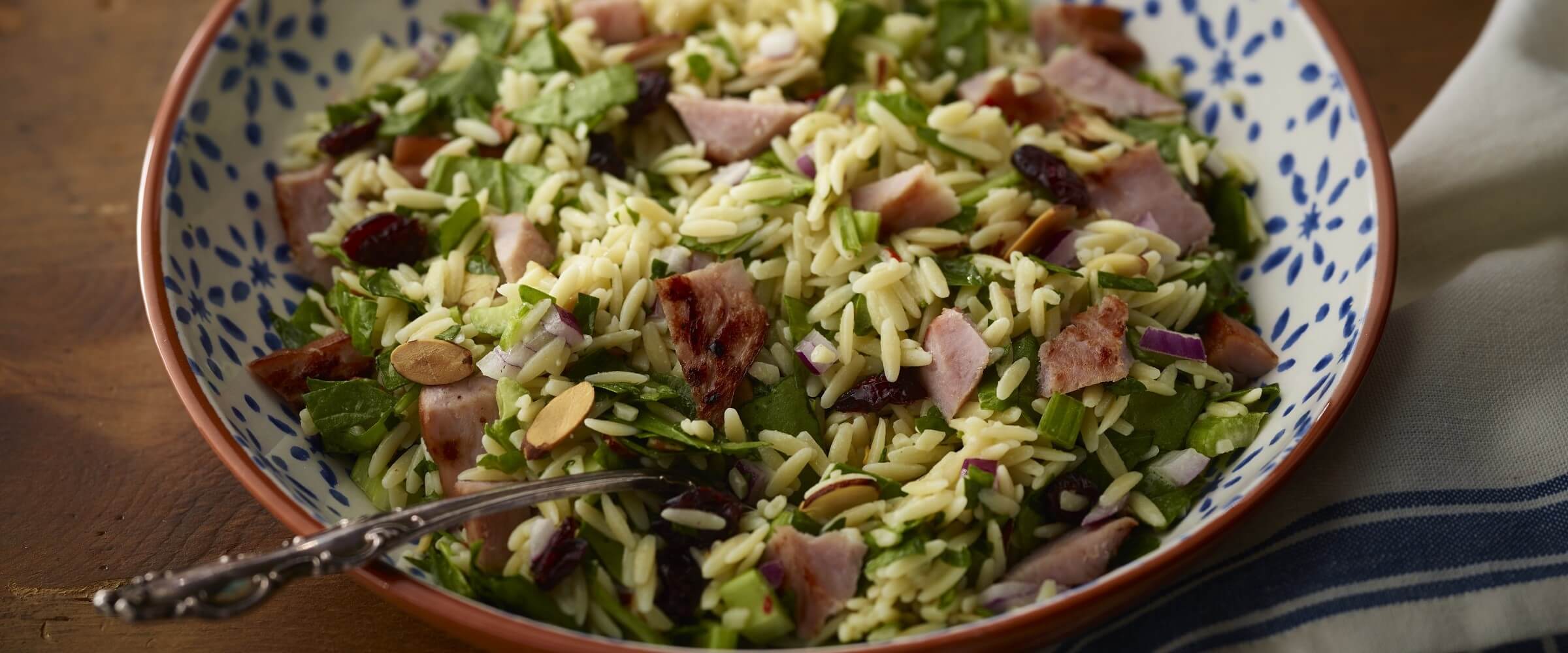 ham and orzo salad in bowl with serving spoon