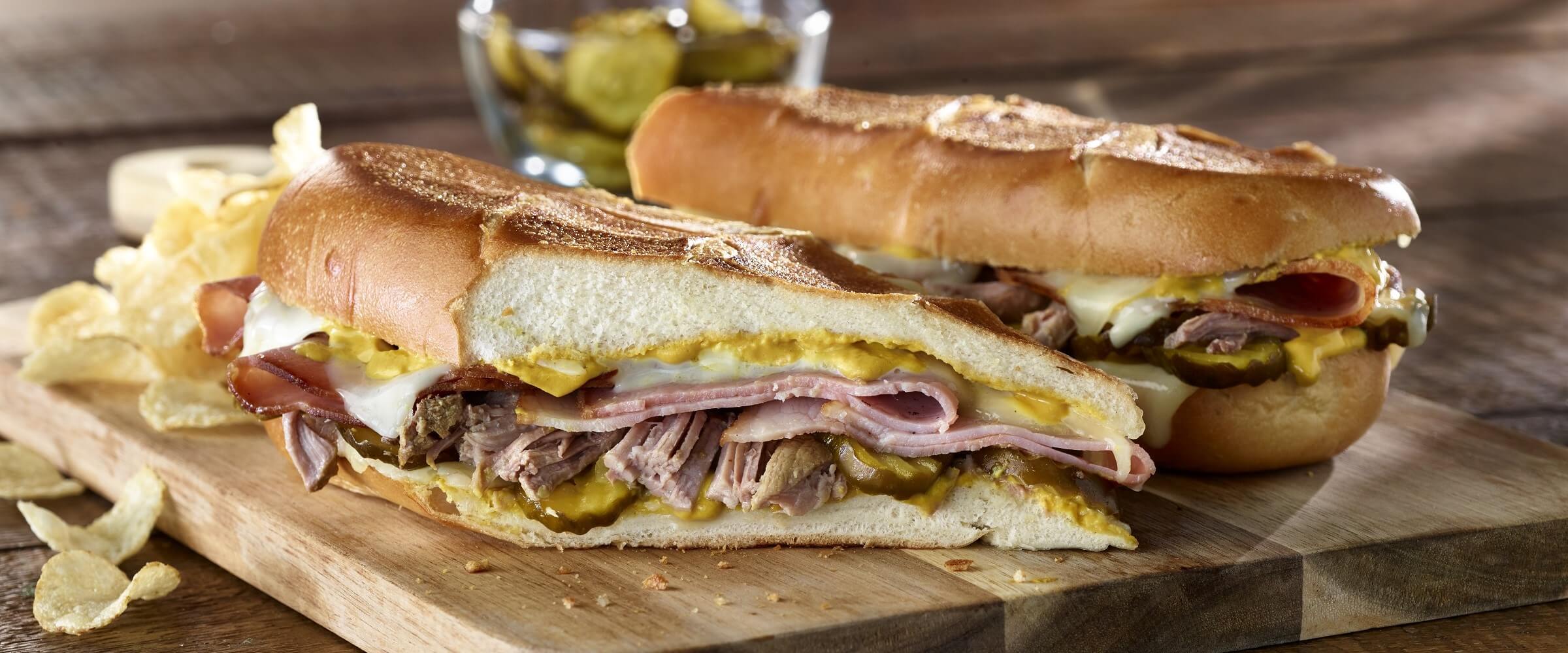 ham cubano sandwich on cutting board with chips on side