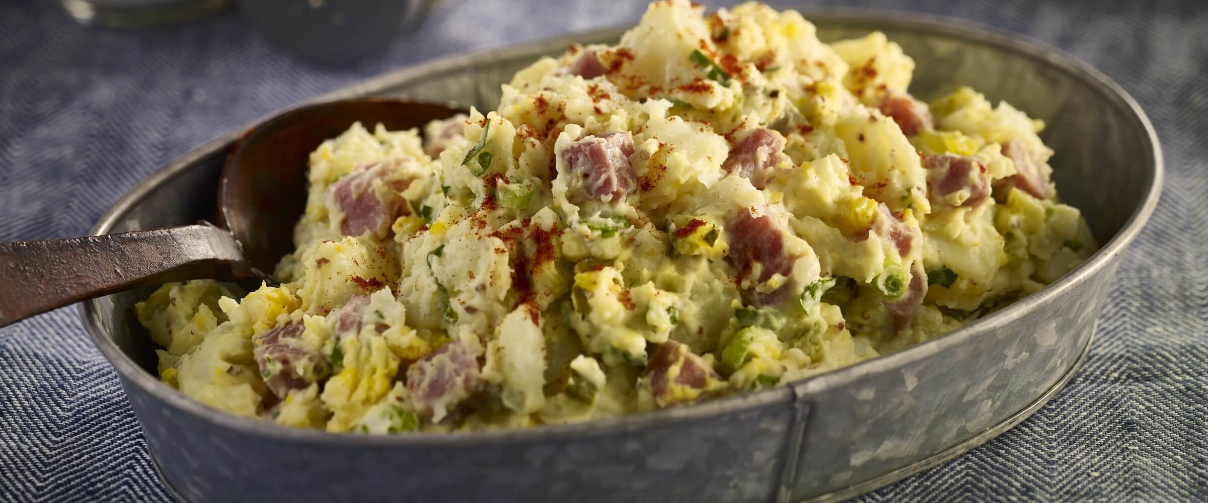 Ham potato salad in tin dish with serving spoon