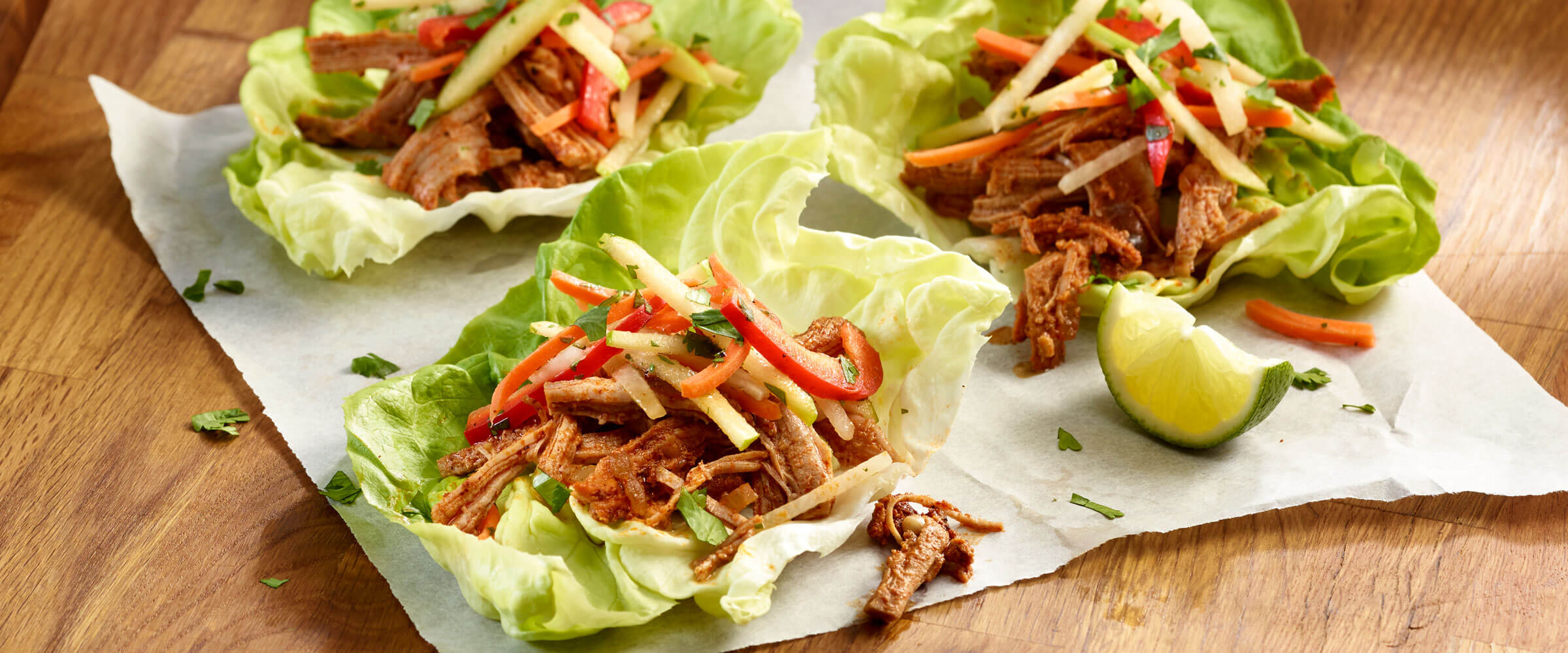 Apple Bourbon Pork Lettuce Wraps with Jicama Slaw on parchment paper with lime wedge