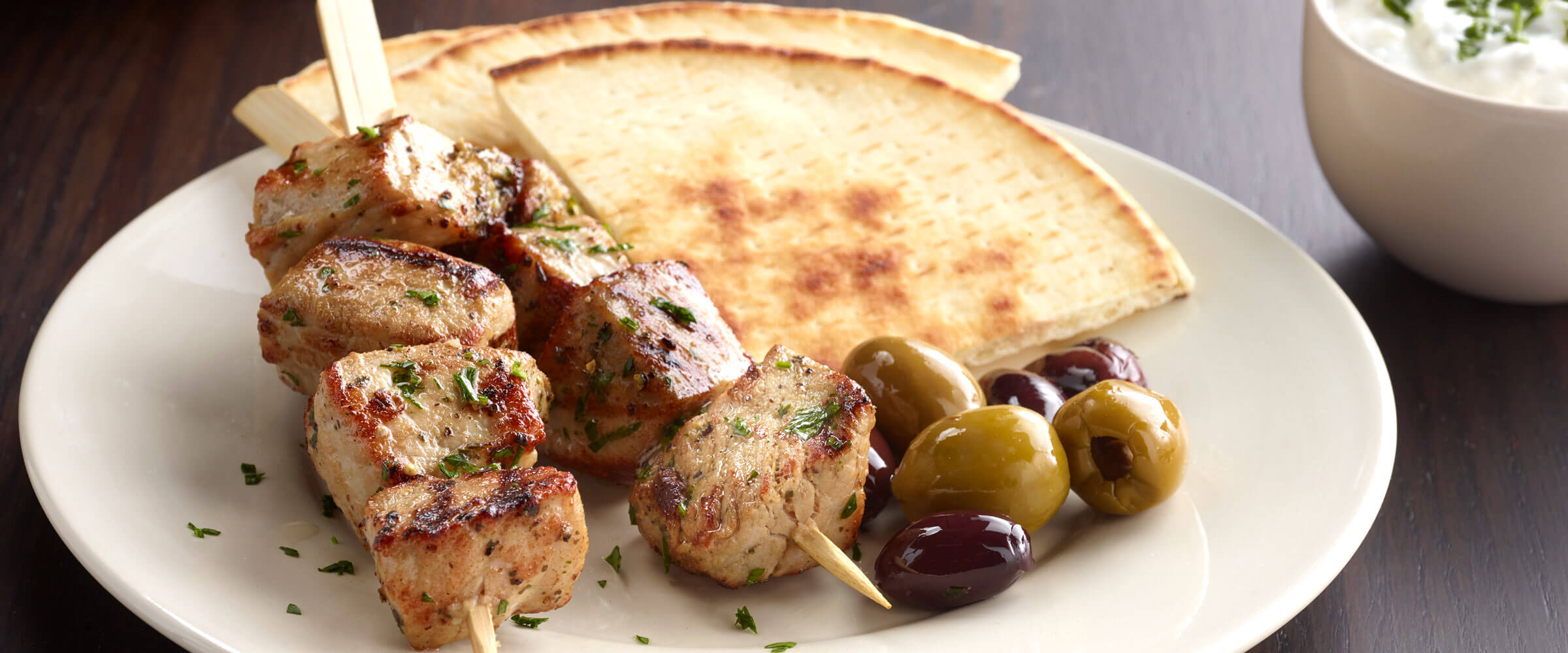 Greek Pork Kabobs with side of pita bread slices and olives on white plate
