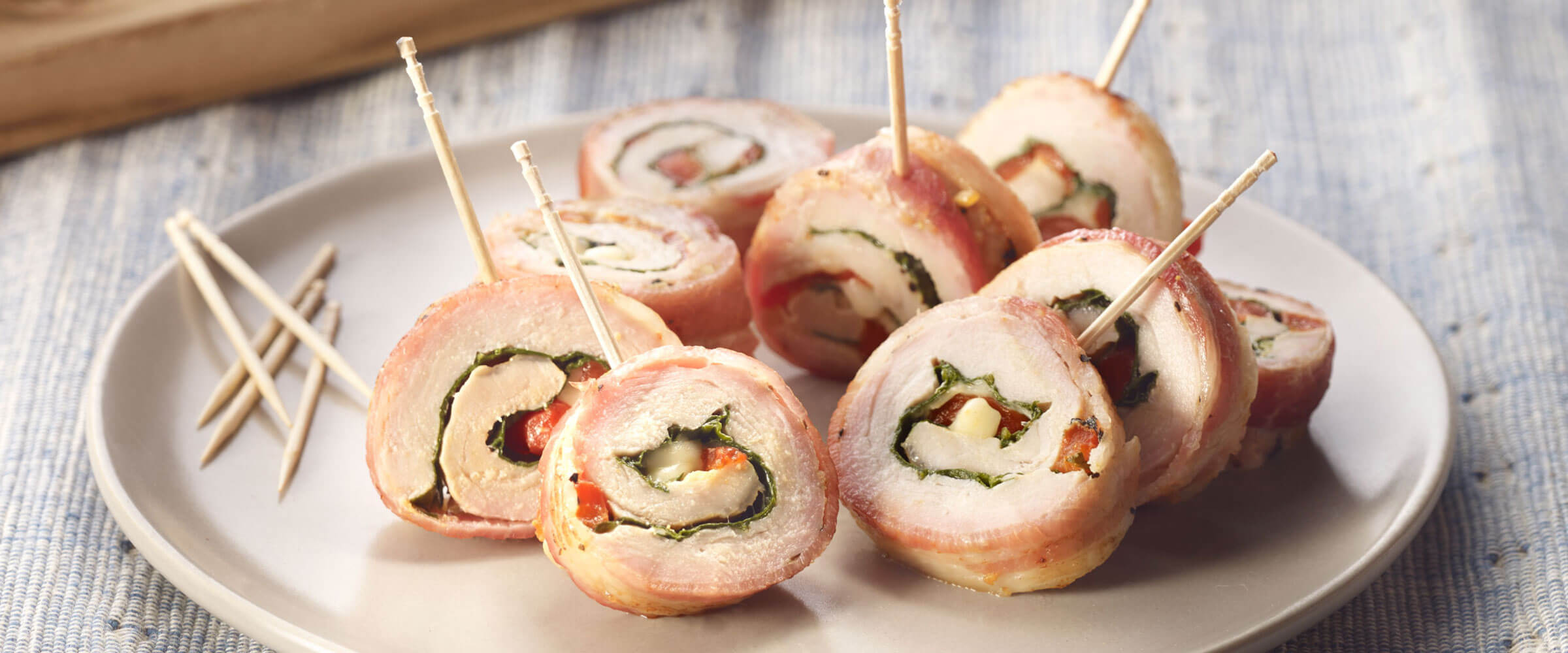Bacon-Wrapped Pork Roll-Ups with toothpicks on plate on blue placemat