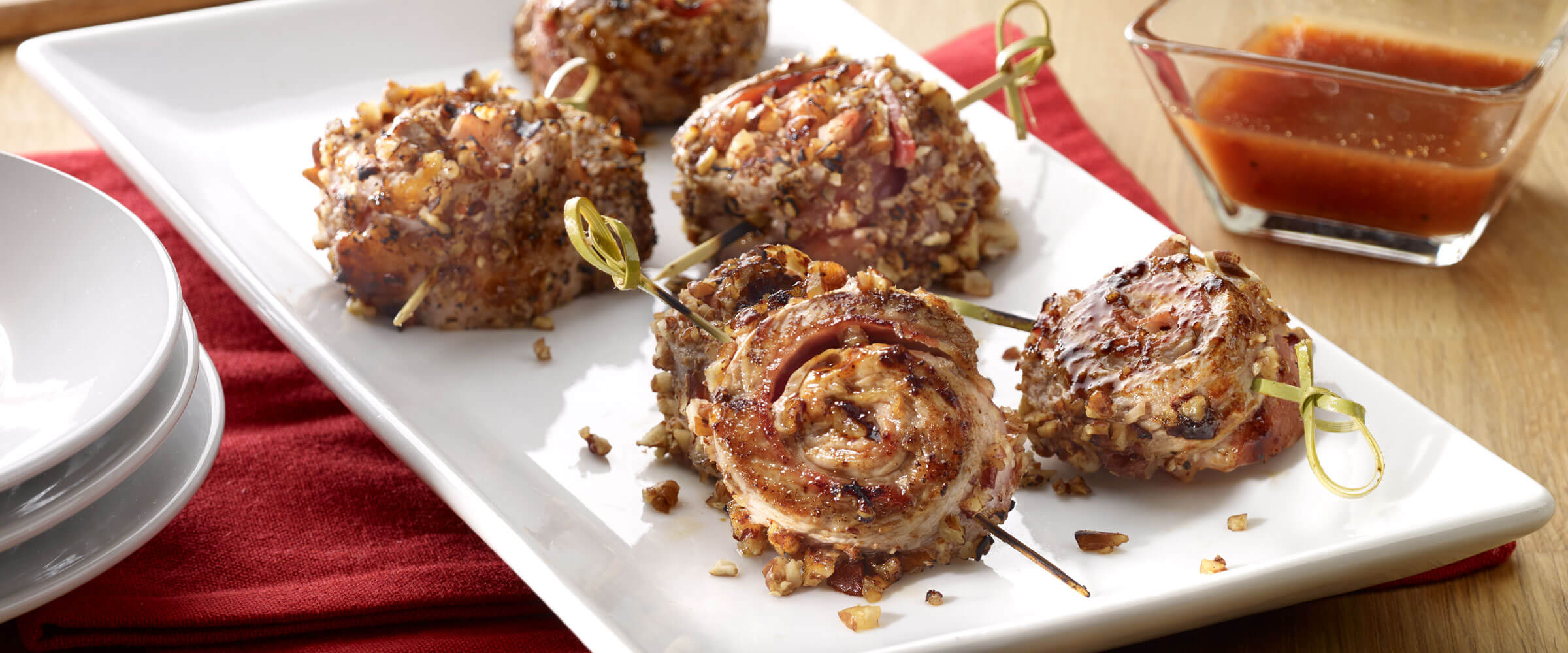 Pecan-Crusted Pork Pinwheels with toothpicks on white plate with dipping sauce