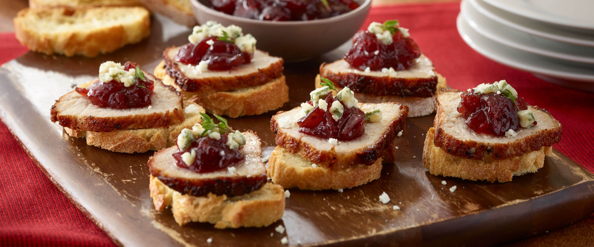 Pork and Apple-Cranberry Chutney Crostini bites on wood board on red tablecloth