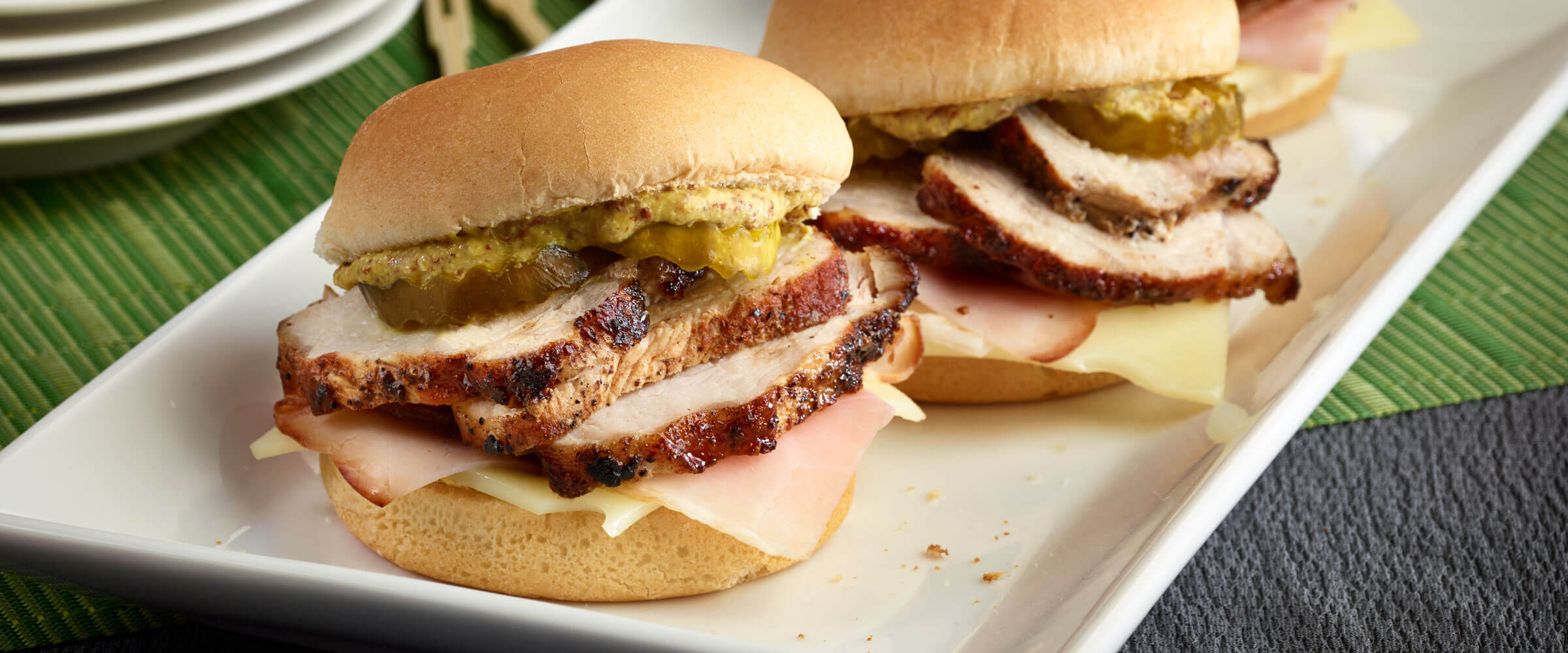 Cubano Sliders topped with pickles and mustard on white platter