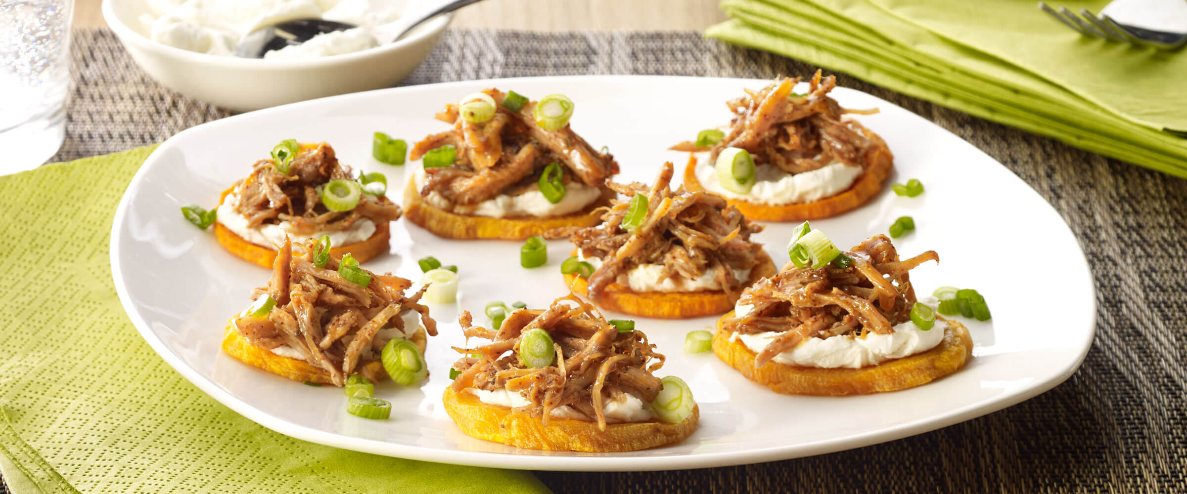 BBQ Pulled Pork Sweet Potato Bites topped with green onions on white plate with green napkin