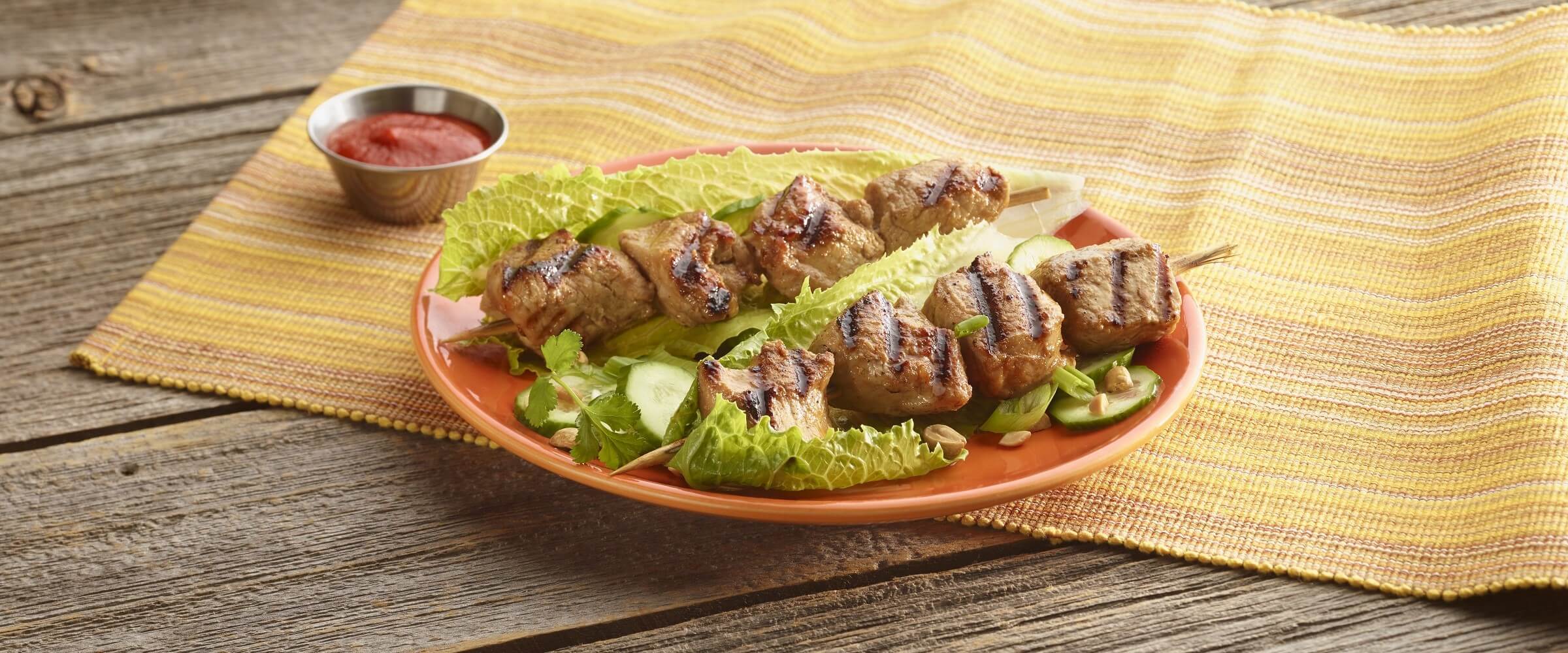 coconut and lime pork kabobs on lettuce leaves on orange plate on yellow placemat