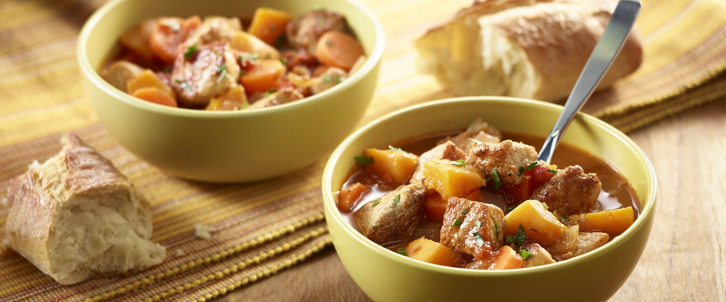 fiesta pork squash soup in yellow bowls with spoon and crusty bread