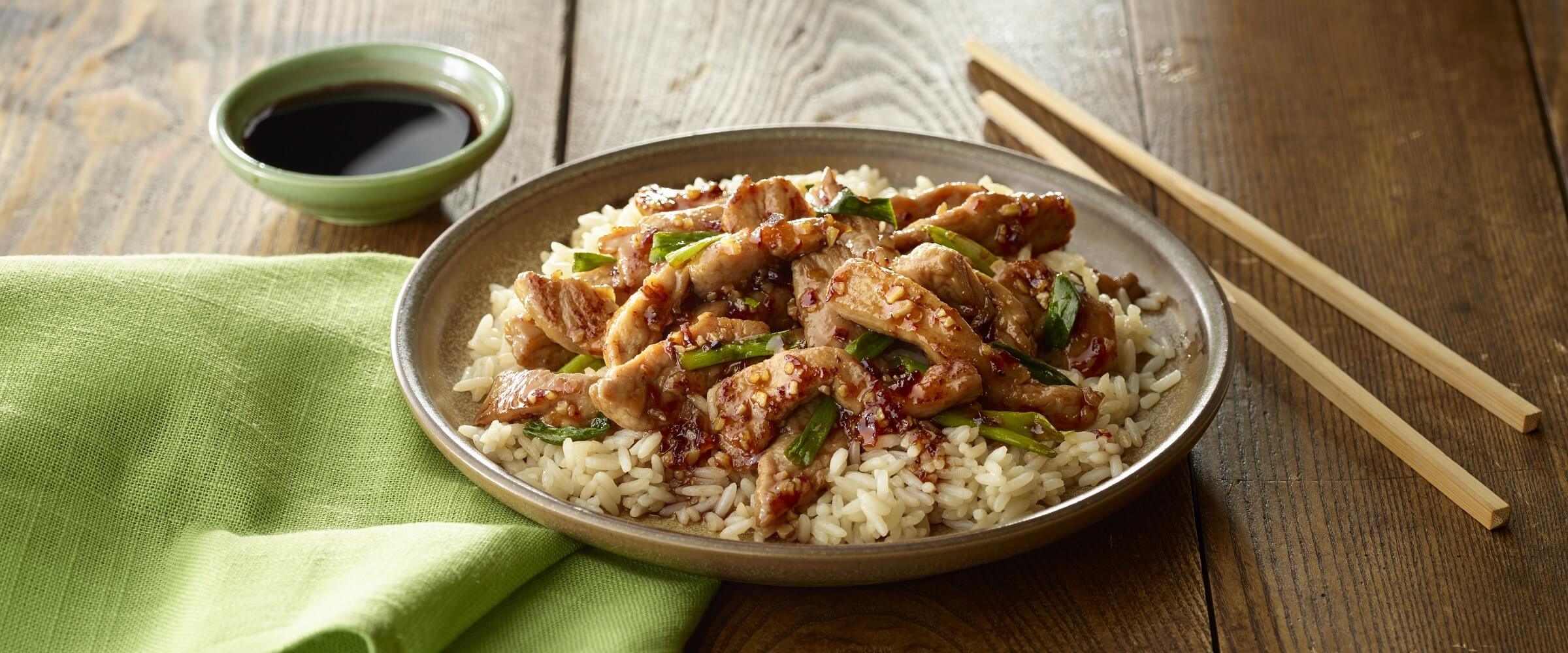 Garlic ginger glazed pork over rice in tan bowl with chopsticks and green napkin