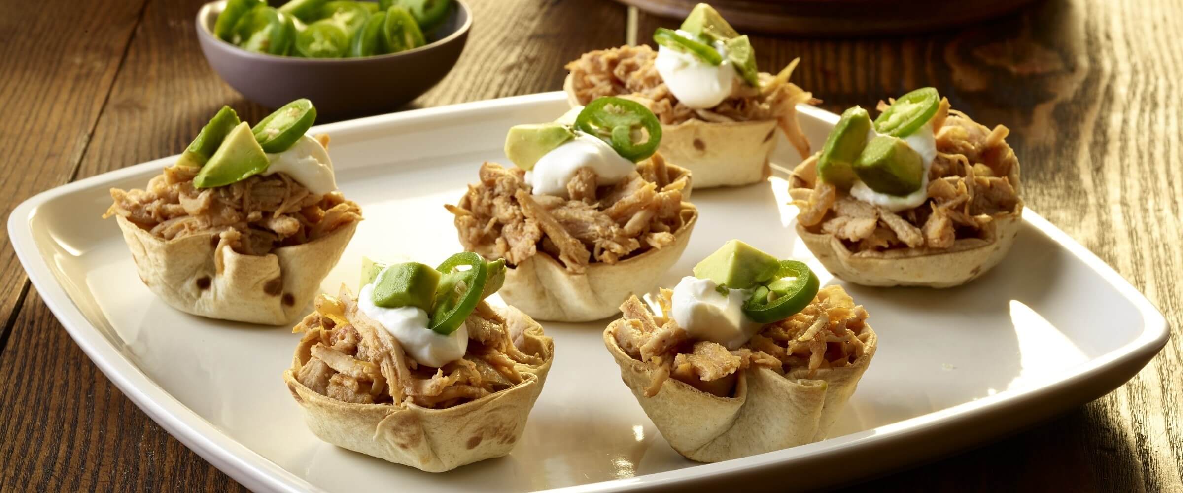 pulled pork wontons topped with sour cream, jalapenos and avocado on white plate