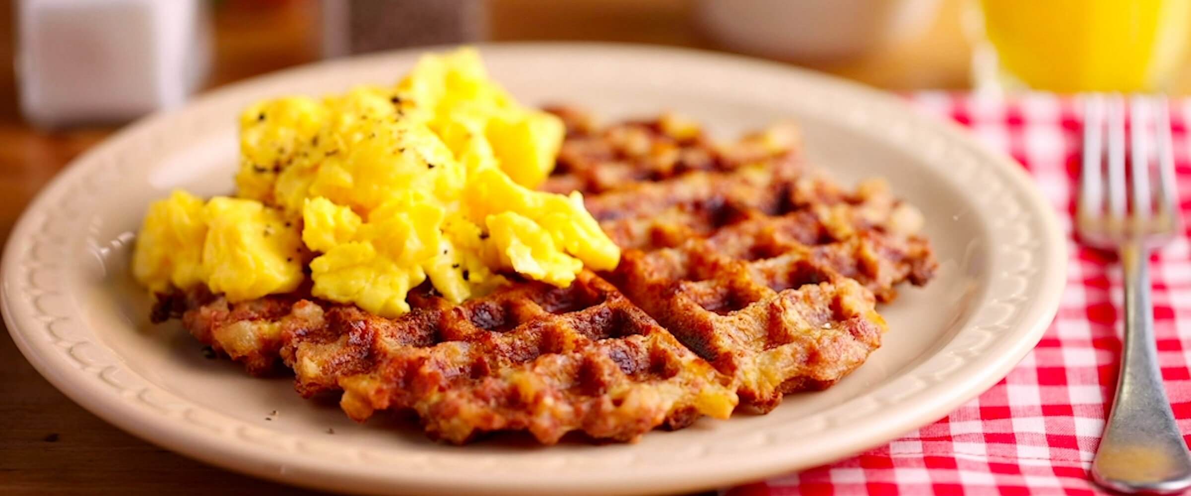 Corned beef hash homestyle waffle with eggs on plate with red and white checkered napkin