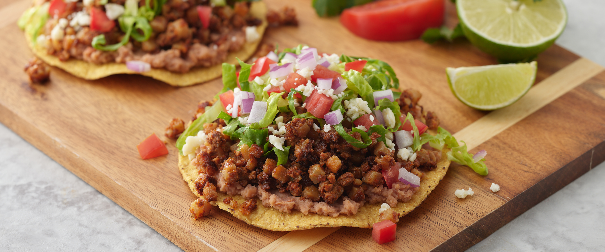 Two Chorizo Skillet Tostadas on a wooden cutting board. Next to the tostadas are wedges of lime.