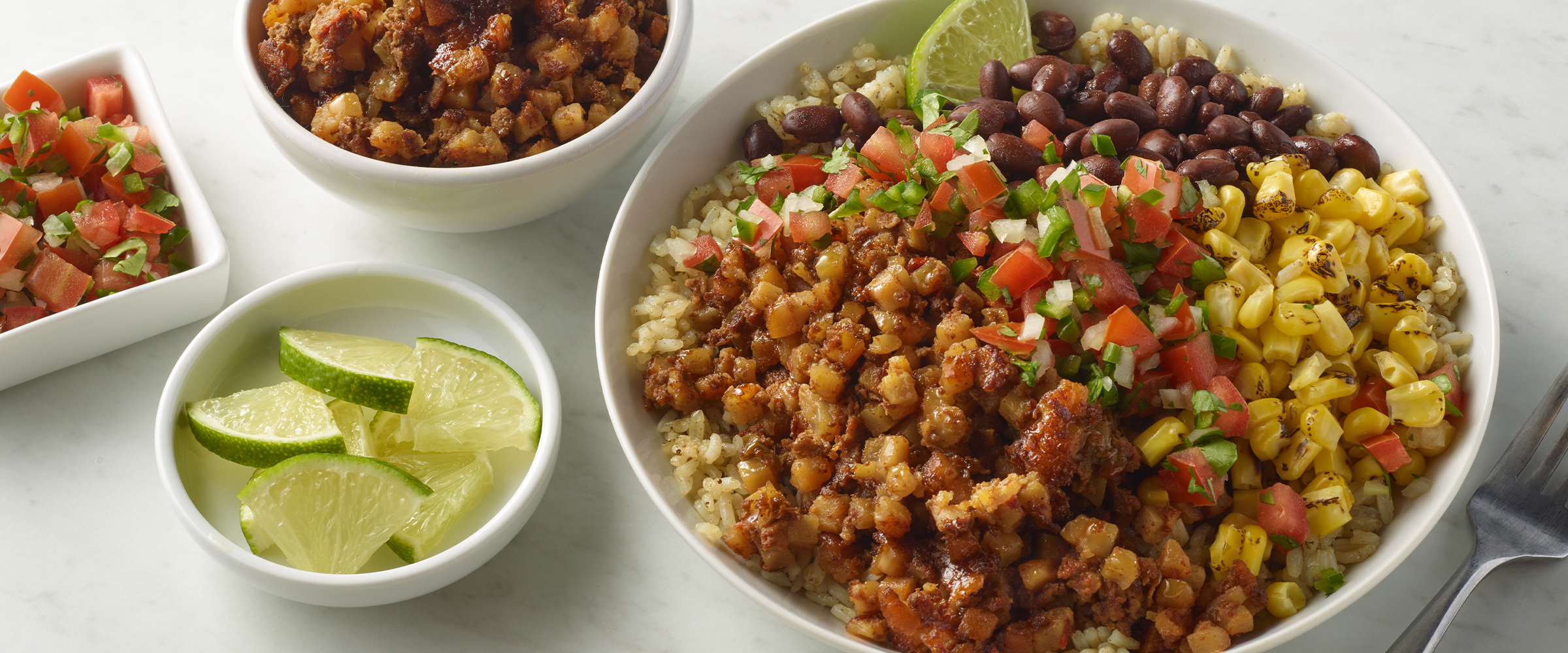 Southwest style grain bowl in a white bowl. Next to the bowl are three small dishes, one has lime wedges and the other two have Pico de Gallo.