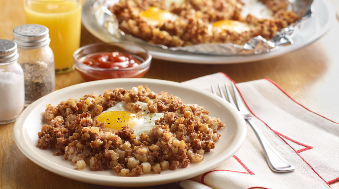 Hash topped with egg on white plate with fork and linen napkin