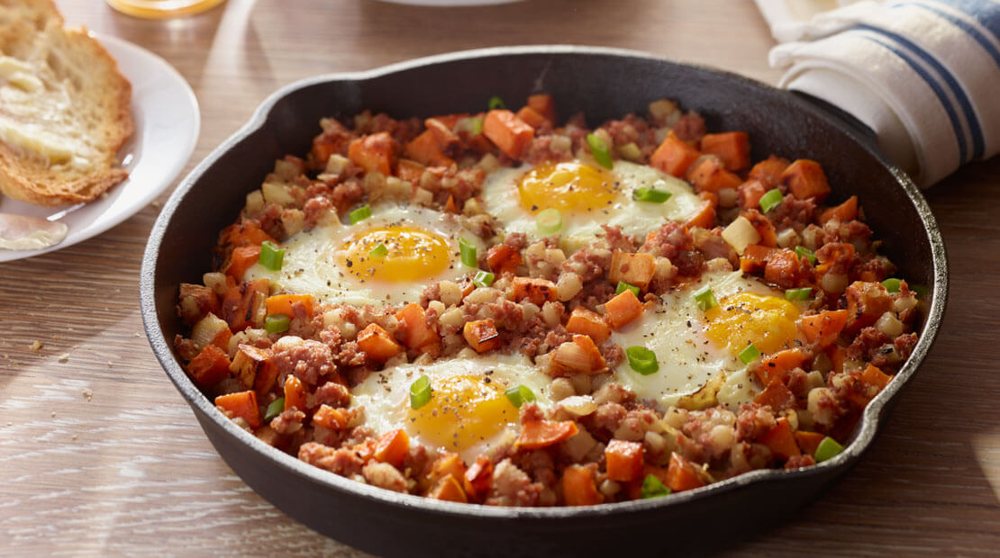 Skillet hash topped with eggs in cast iron skillet with crusty bread