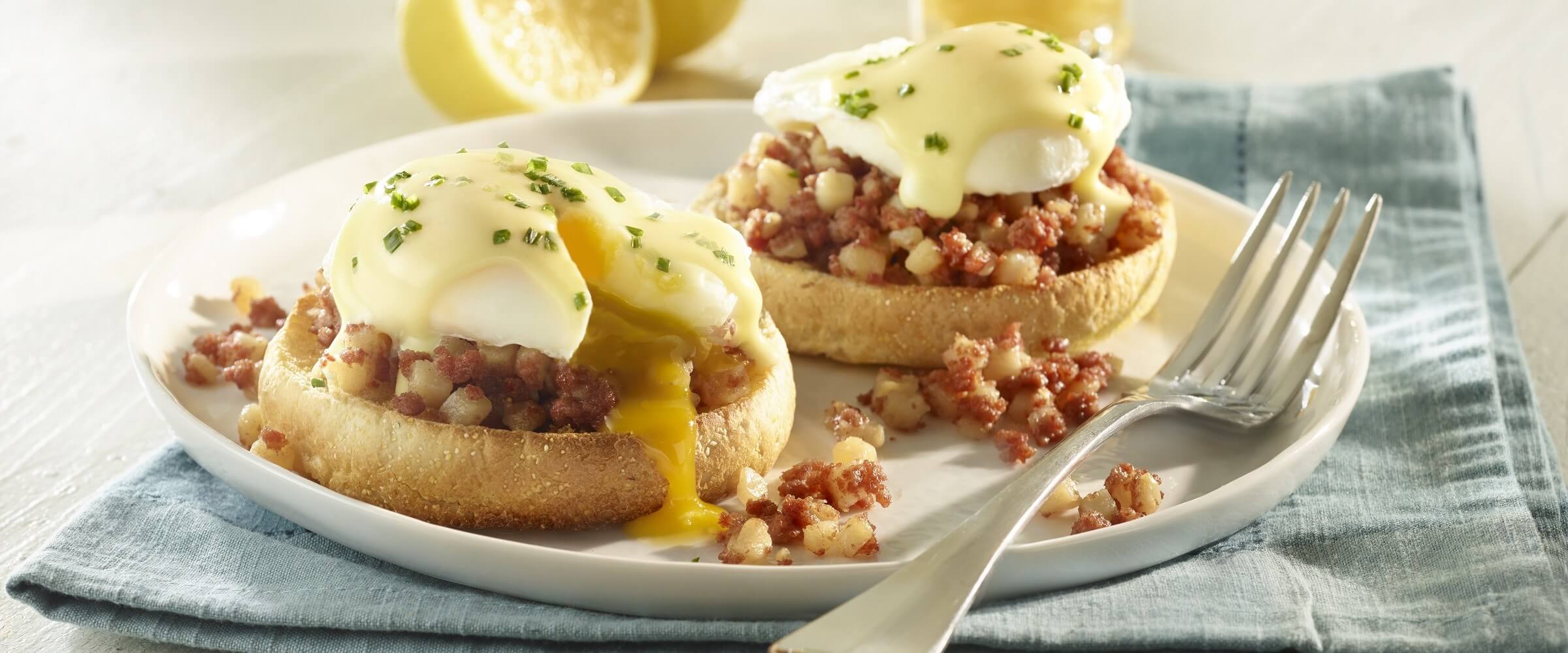 Corned beef hash eggs benedict on white plate with blue linen napkin