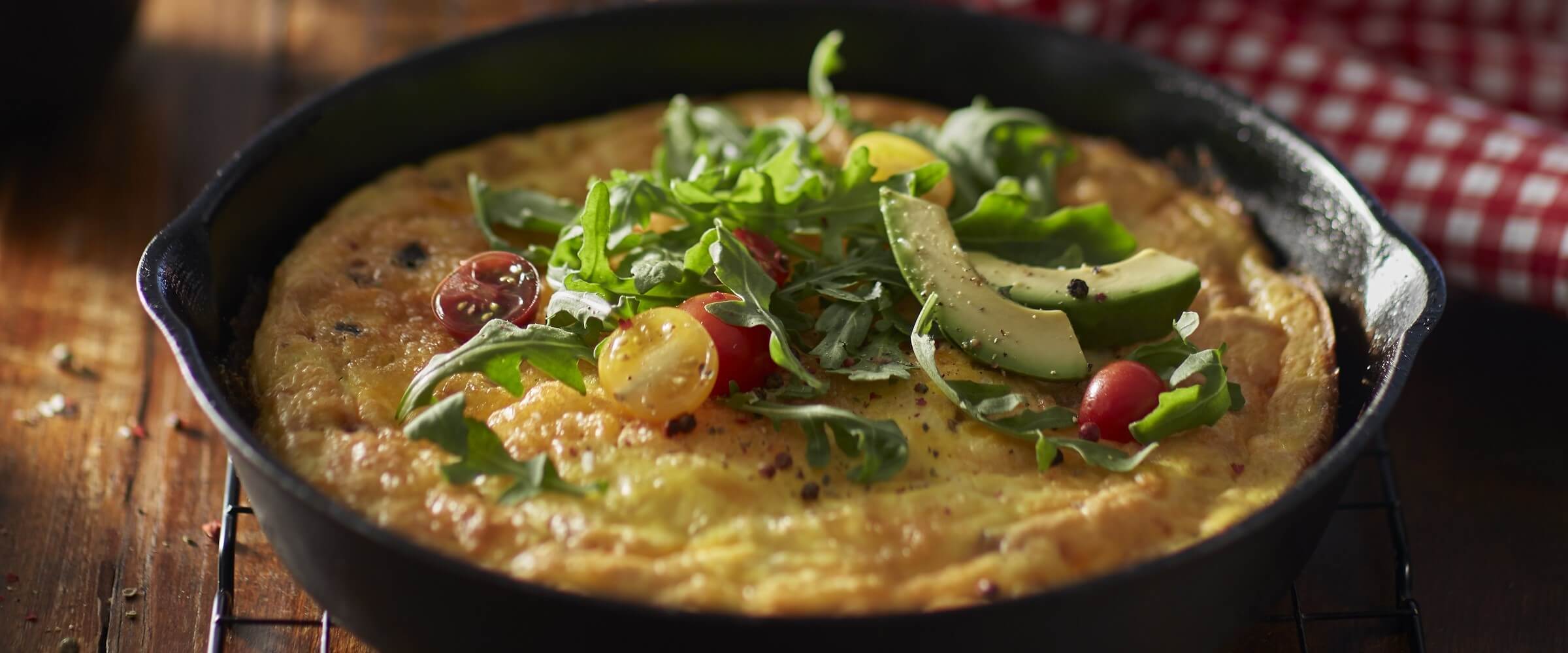 Corned beef frittata in cast iron skillet topped with greens and avocado
