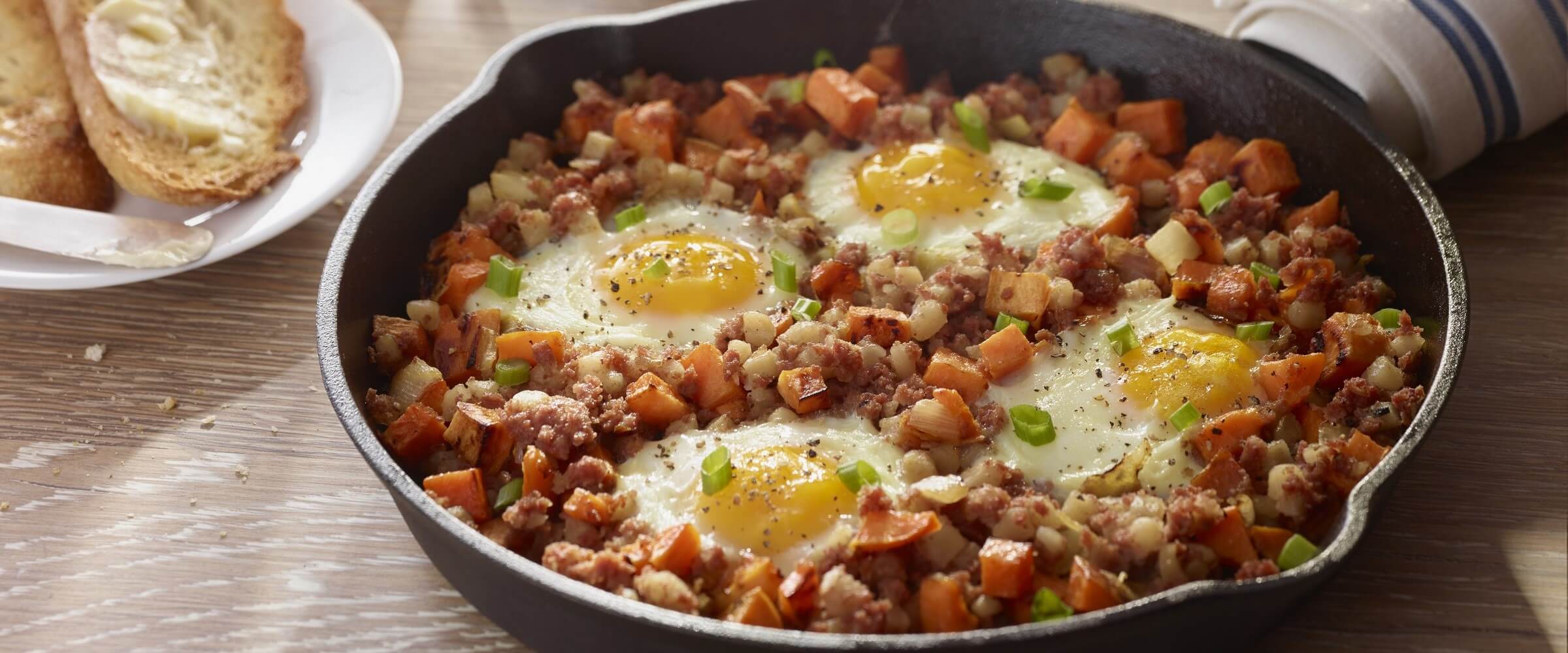 Corned beef sweet potato breakfast hash in cast iron skillet topped with eggs