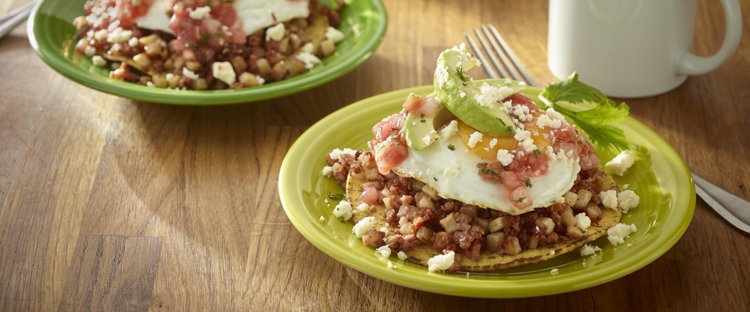 Hash breakfast tostada on green plate topped with egg and avocado