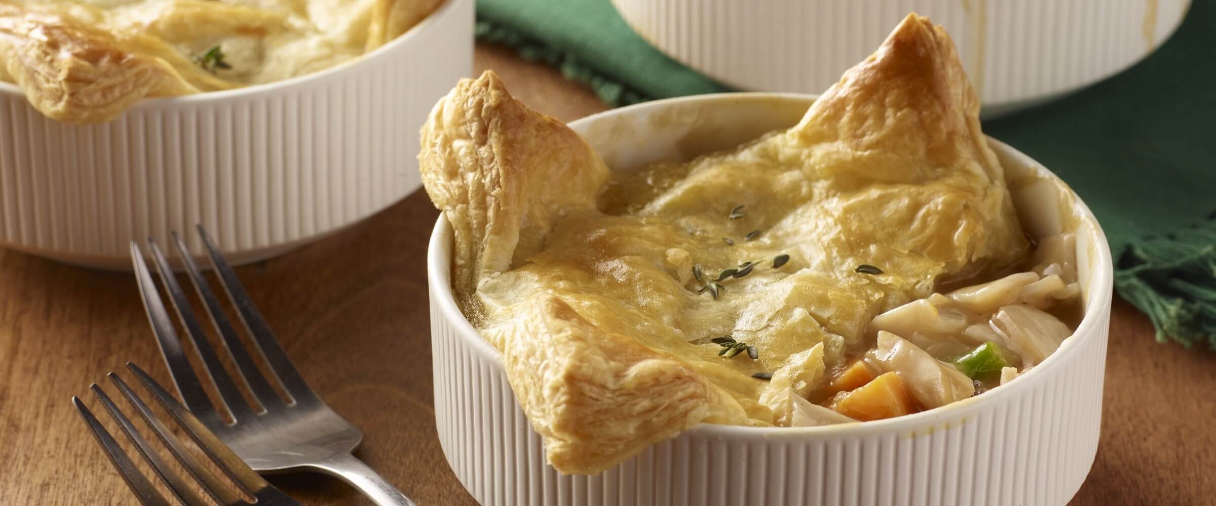 individual puff pastry turkey pot pie in white bowls with forks