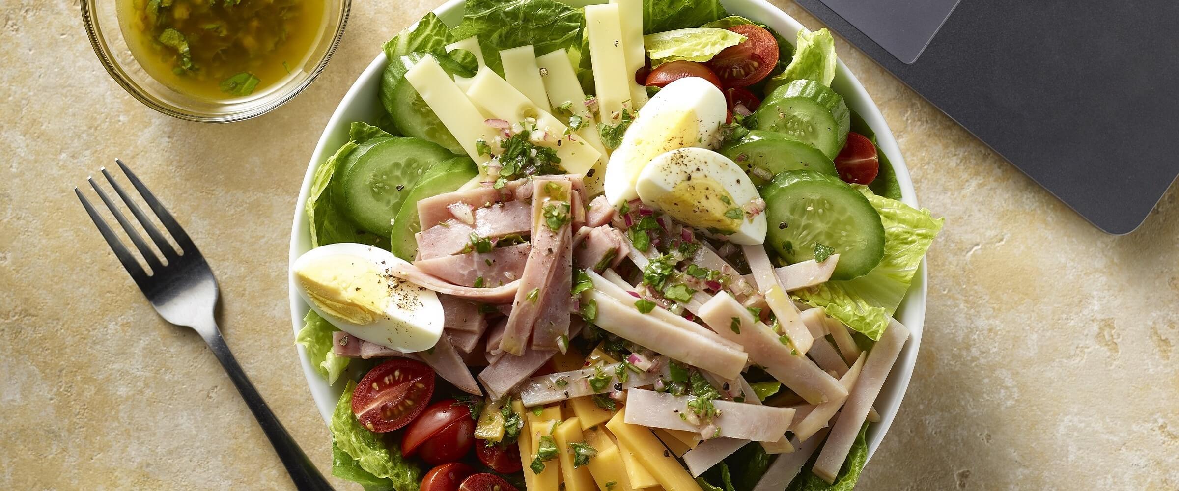 Chef salad in white bowl with dressing on the side