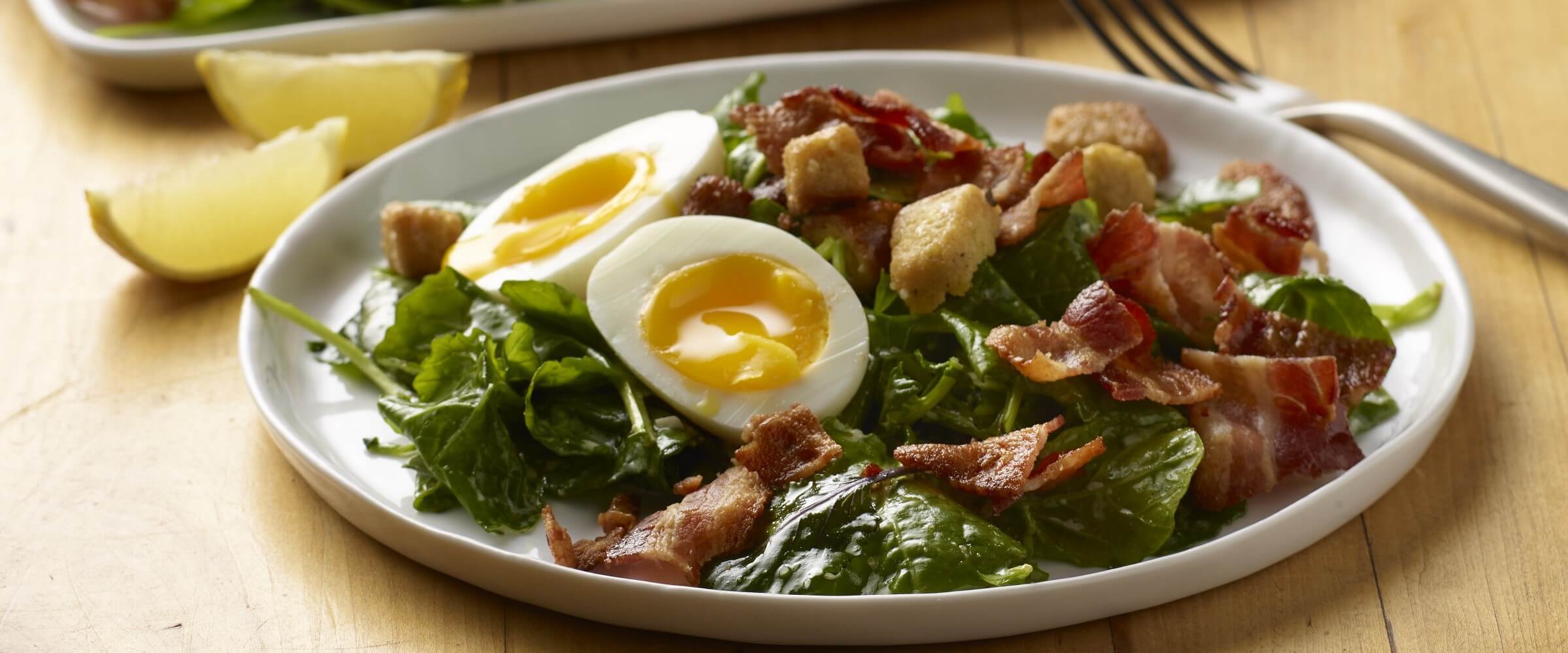 kale caesar salad with egg and bacon on white plate with lemon wedges