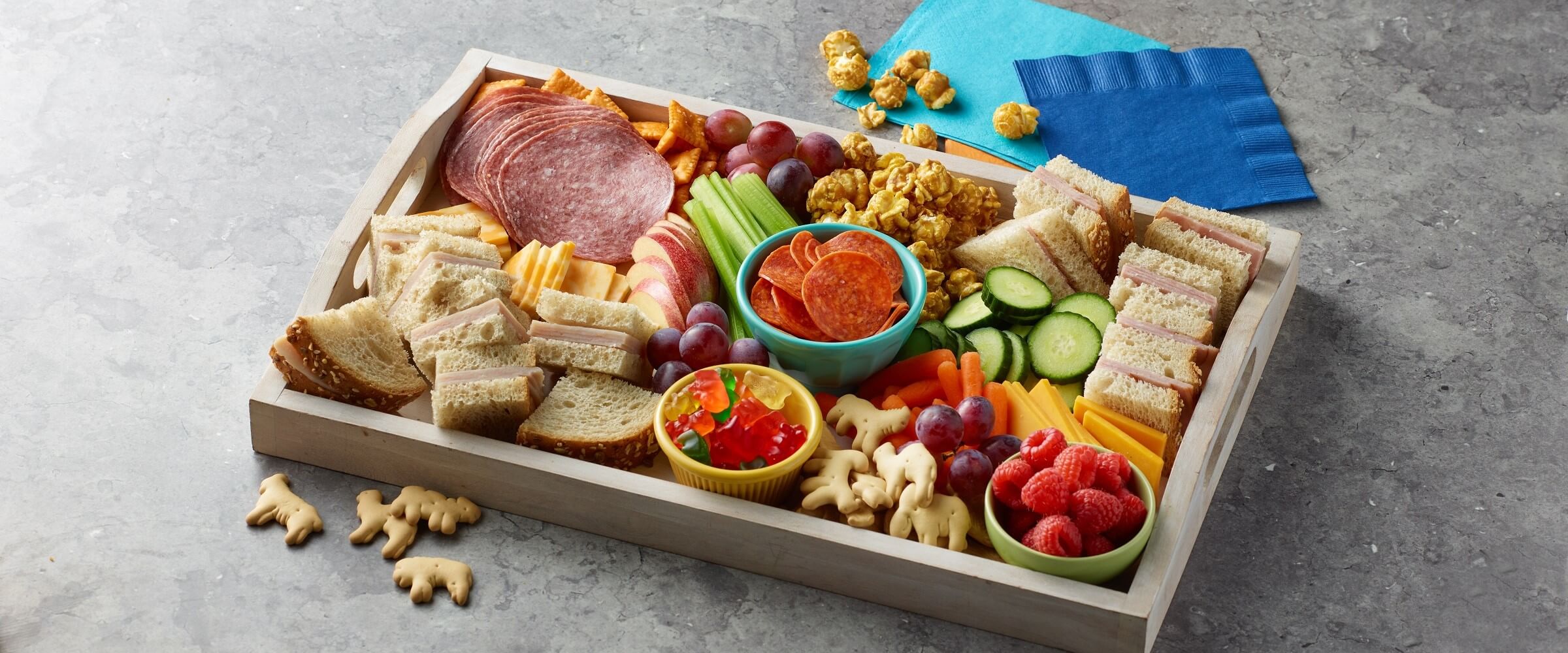 Kids charcuterie board with mini sandwiches, crackers, meat, cheese, popcorn, fruit and gummy bears