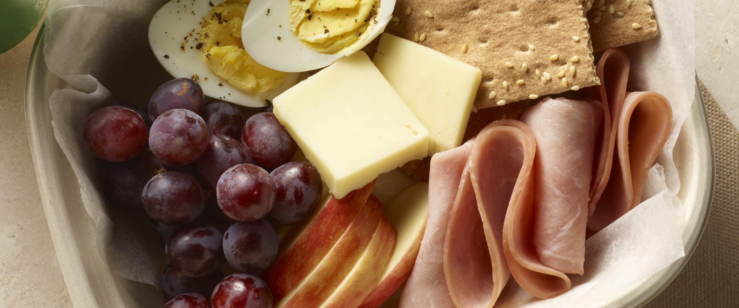 protein box with meat, cheese, eggs, crackers, grapes and apples