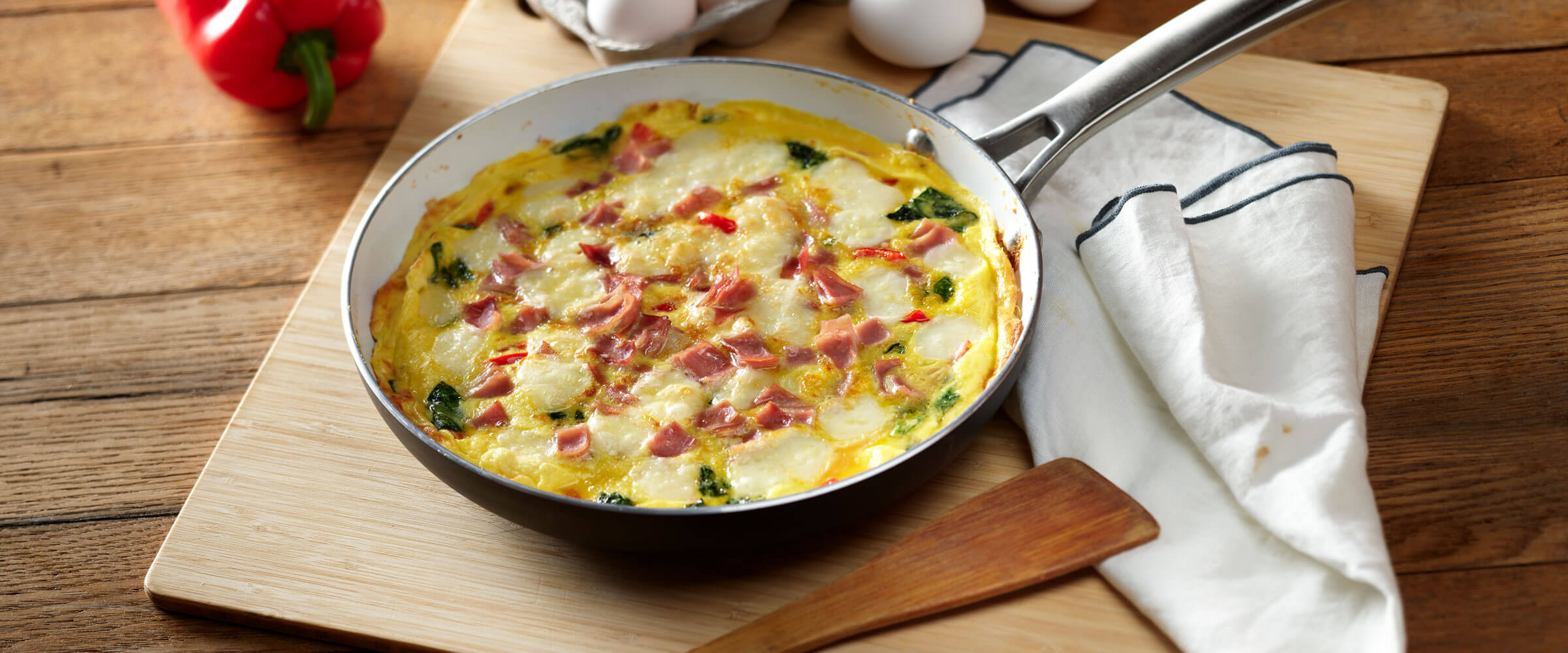 Ham and Fontina Frittata in skillet on wooden cutting board with linen napkin