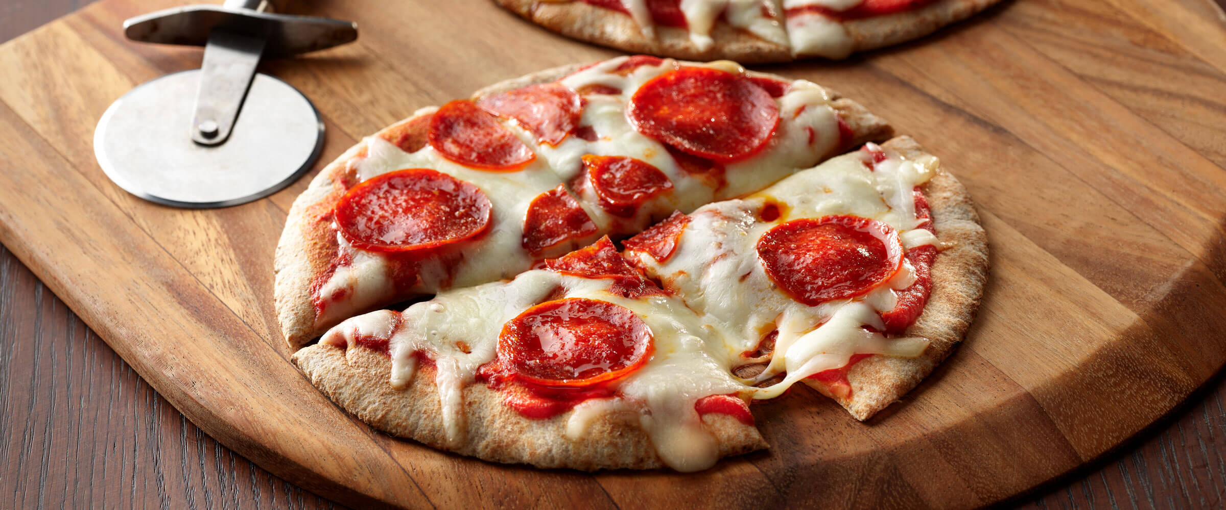 Pepperoni Pita Pizza sliced on wooden board with pizza cutter