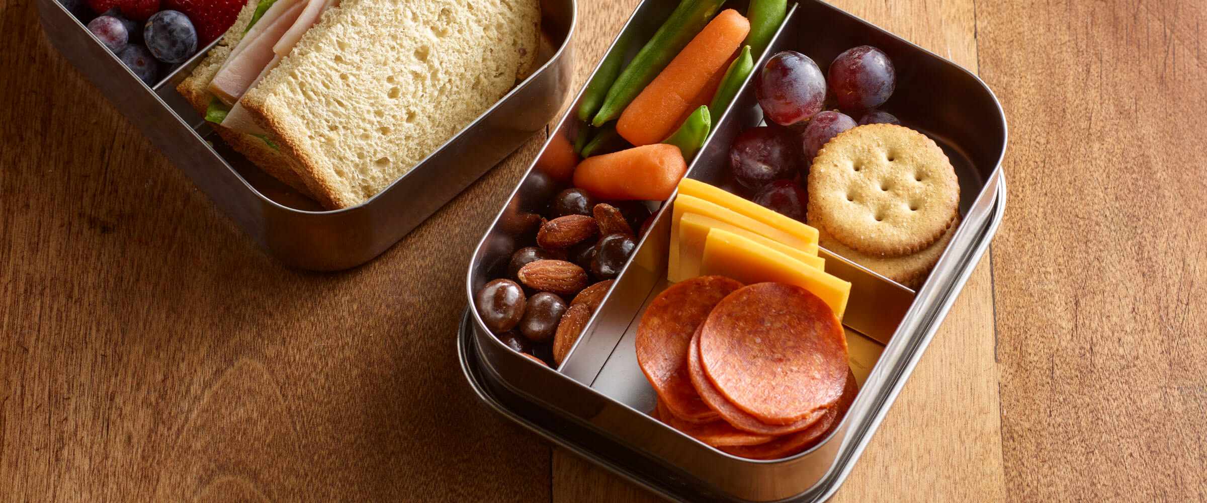 Pepperoni Bento Boxes with cheese, crackers, grapes, veggies and nuts on wooded table