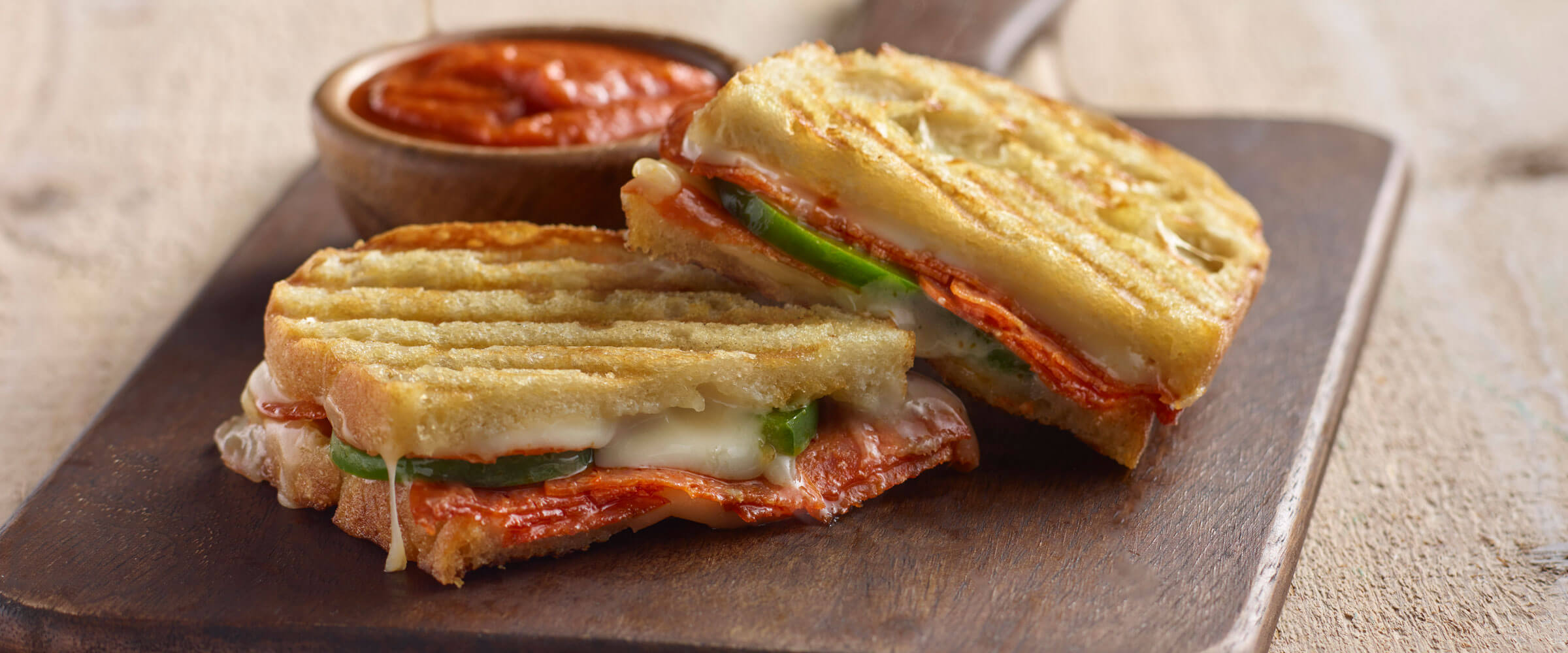 Pepperoni and Mozzarella Panini on wood board with bowl of dipping sauce
