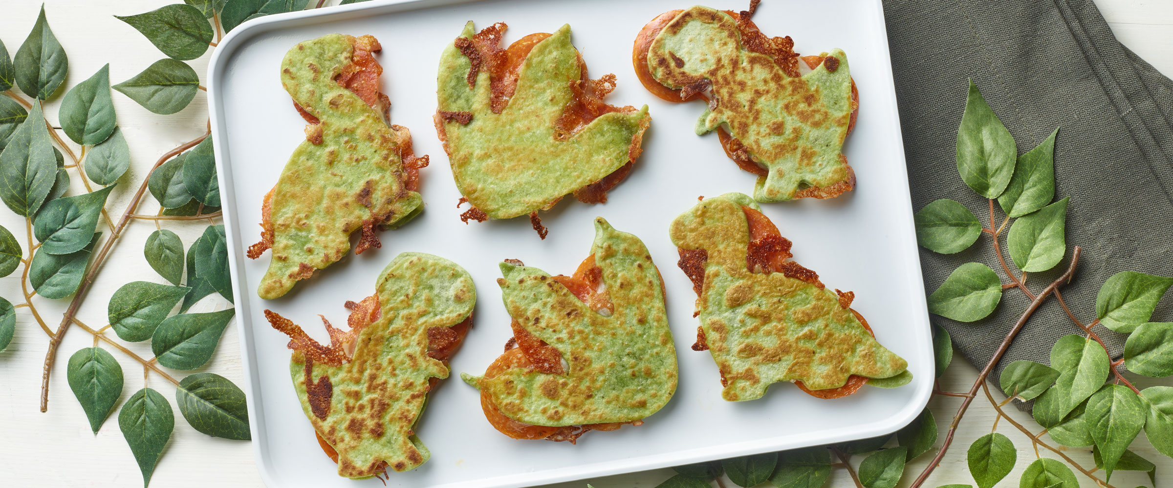 Pepperoni Dino Quesadillas on white plate with decorative greens